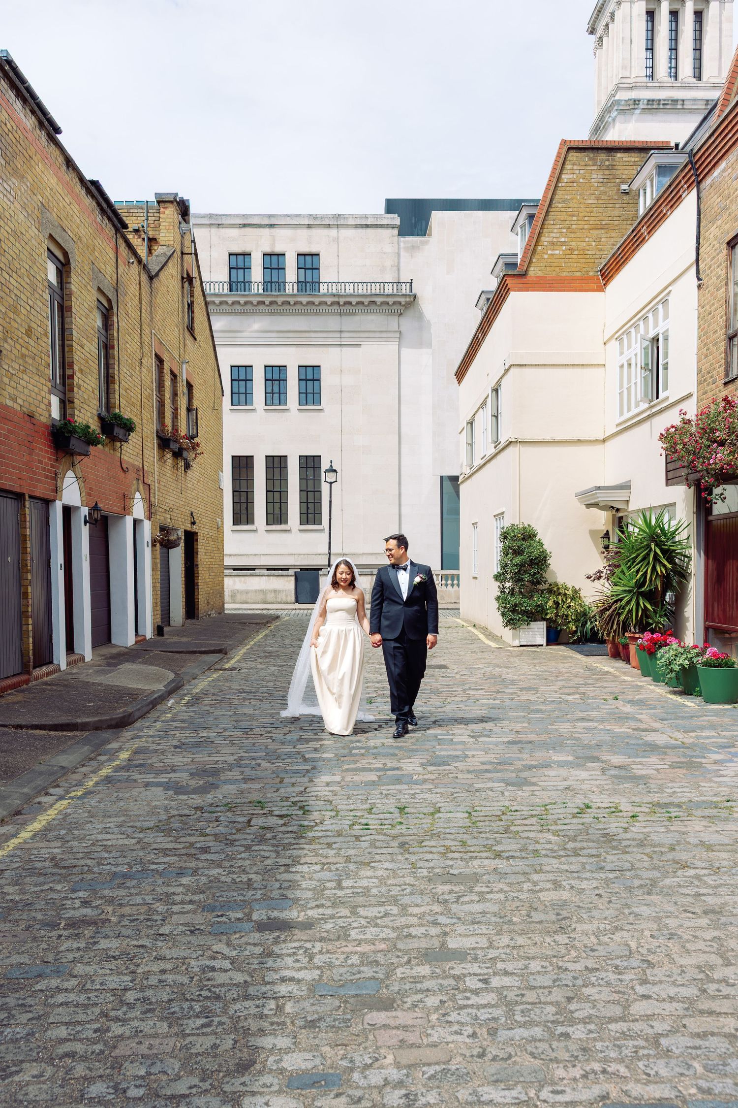 Bride and groom walking together down charming cobblestone London mews street after wedding.