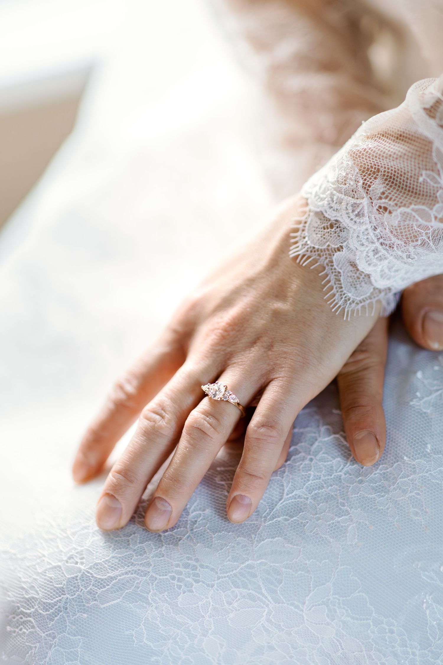 Delicate lace details on wedding dress sleeve with engagement ring visible.