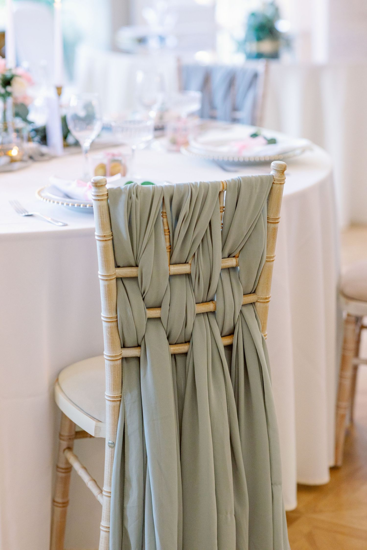 Elegant sage green fabric draped decoratively on white chiavari chairs at a formal event setting.