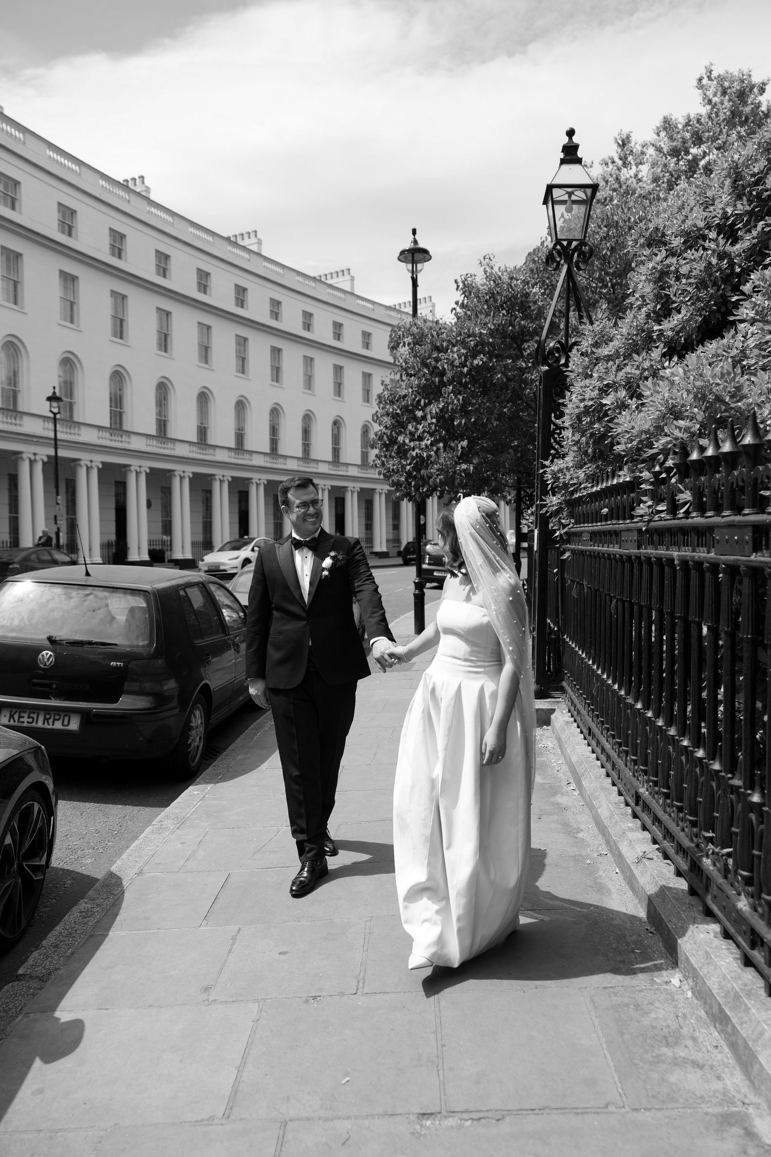Black and white photo of bride and groom walking hand in hand along a London street.