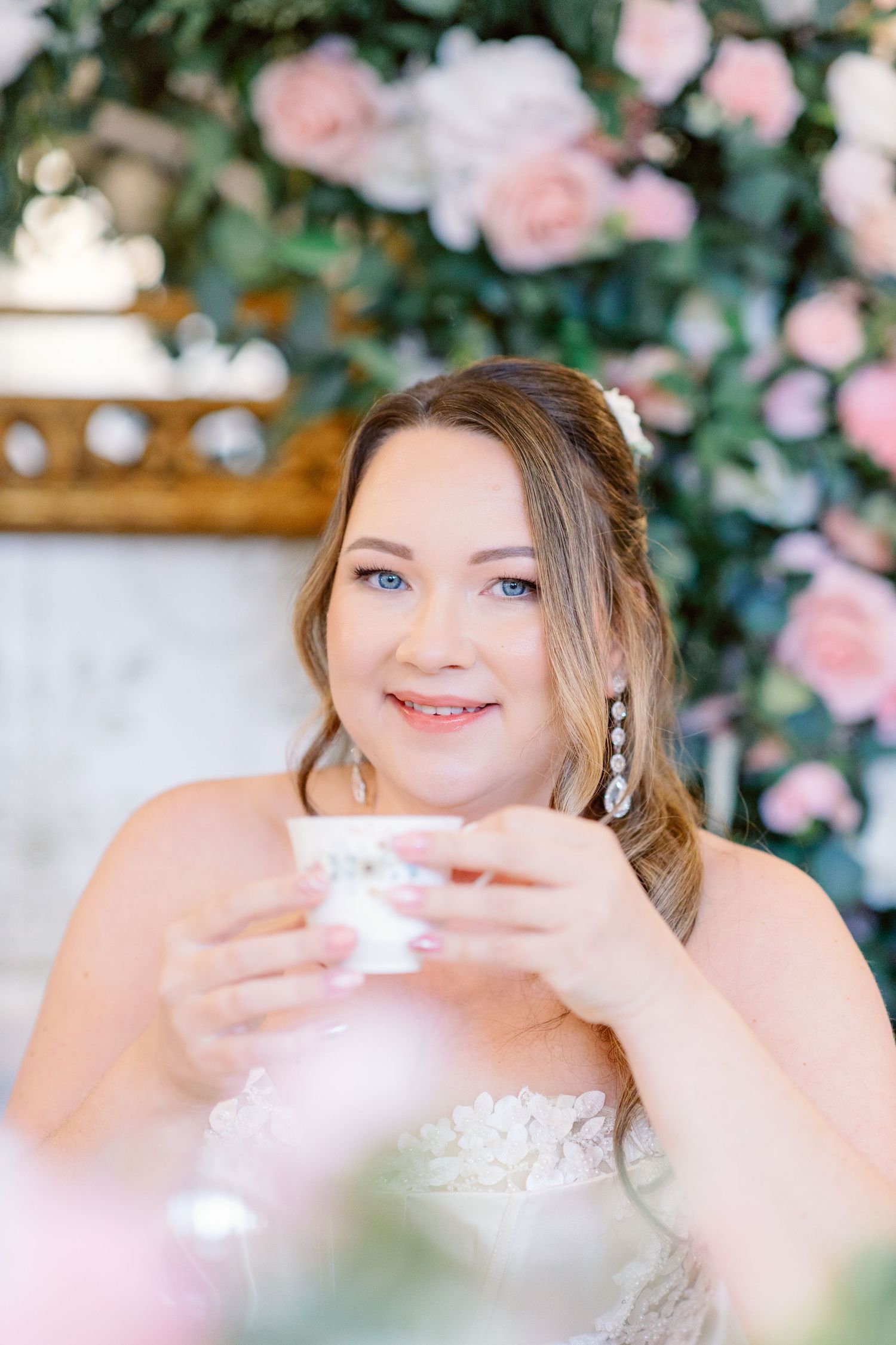 Elegant wedding scene with pink roses and a delicate teacup against a floral backdrop.