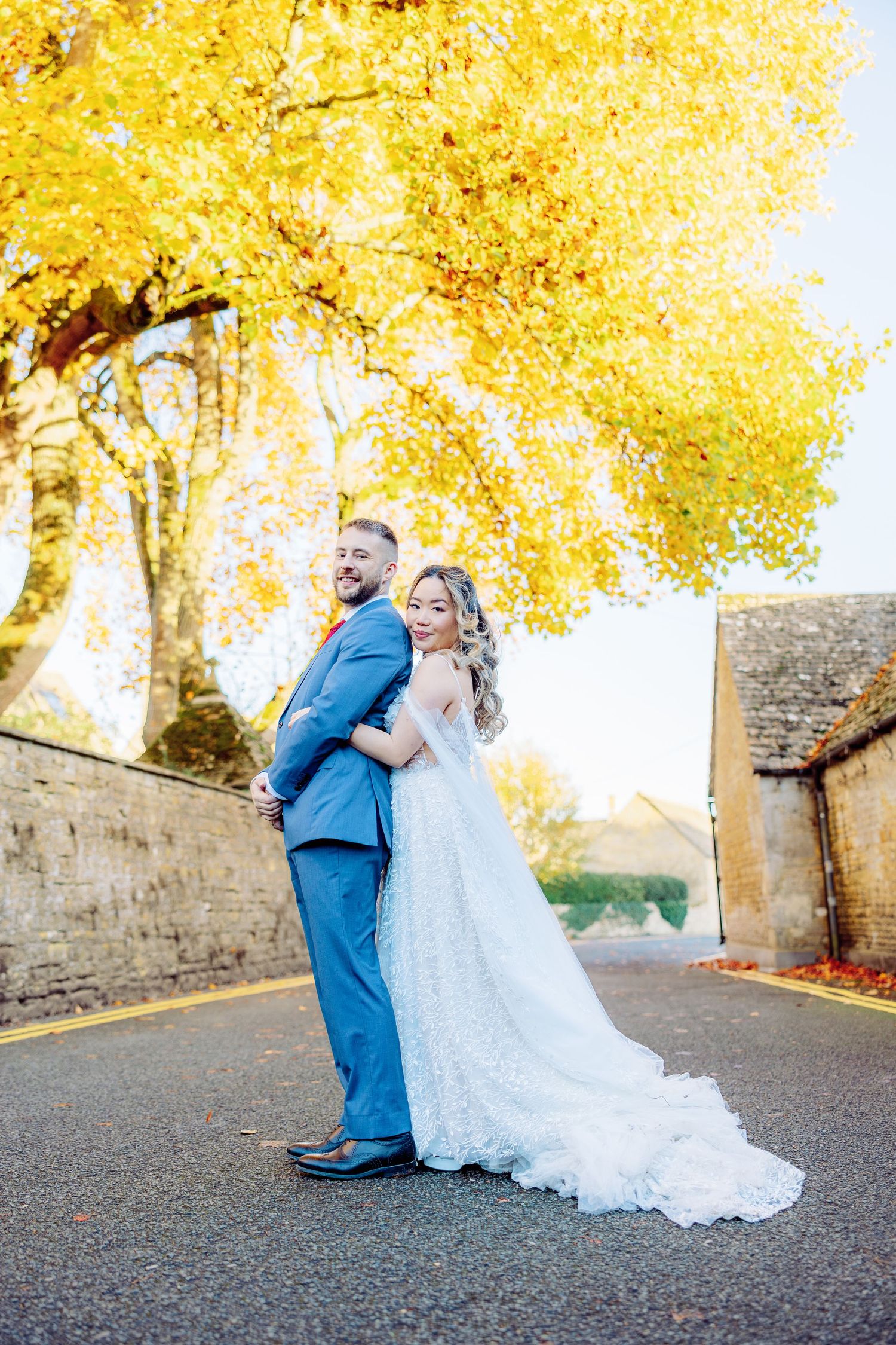 Couple in wedding attire posing under golden autumn trees.