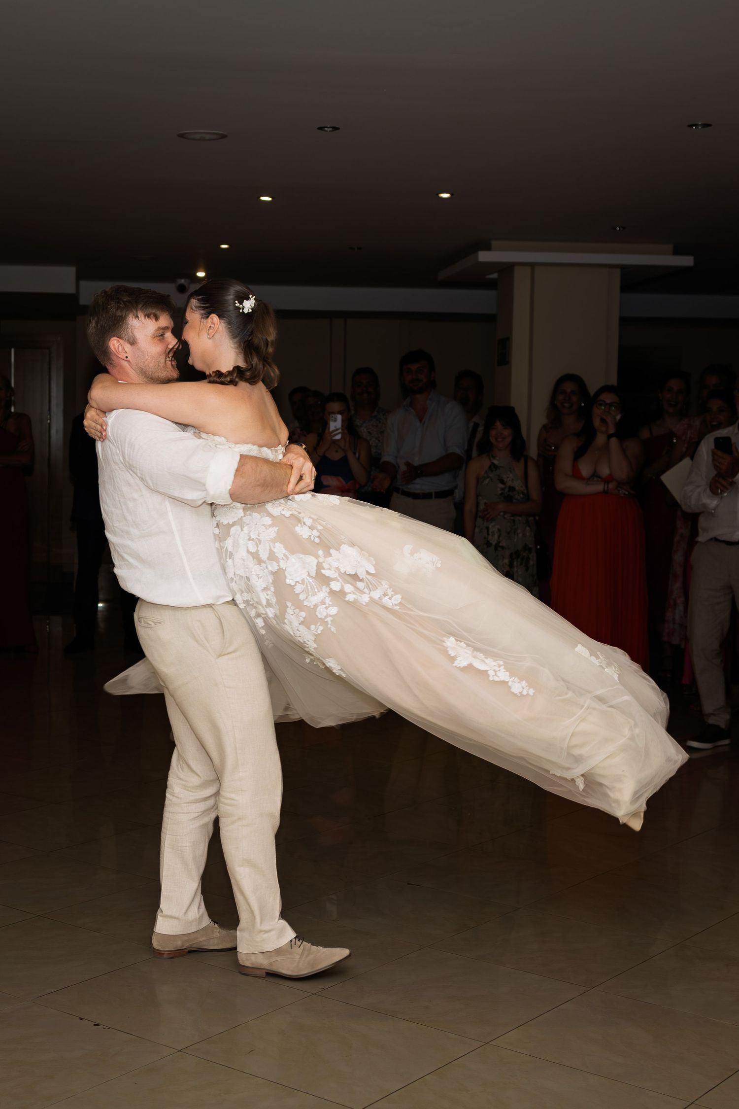 Groom lifting bride in lace wedding gown during first dance at elegant wedding reception.