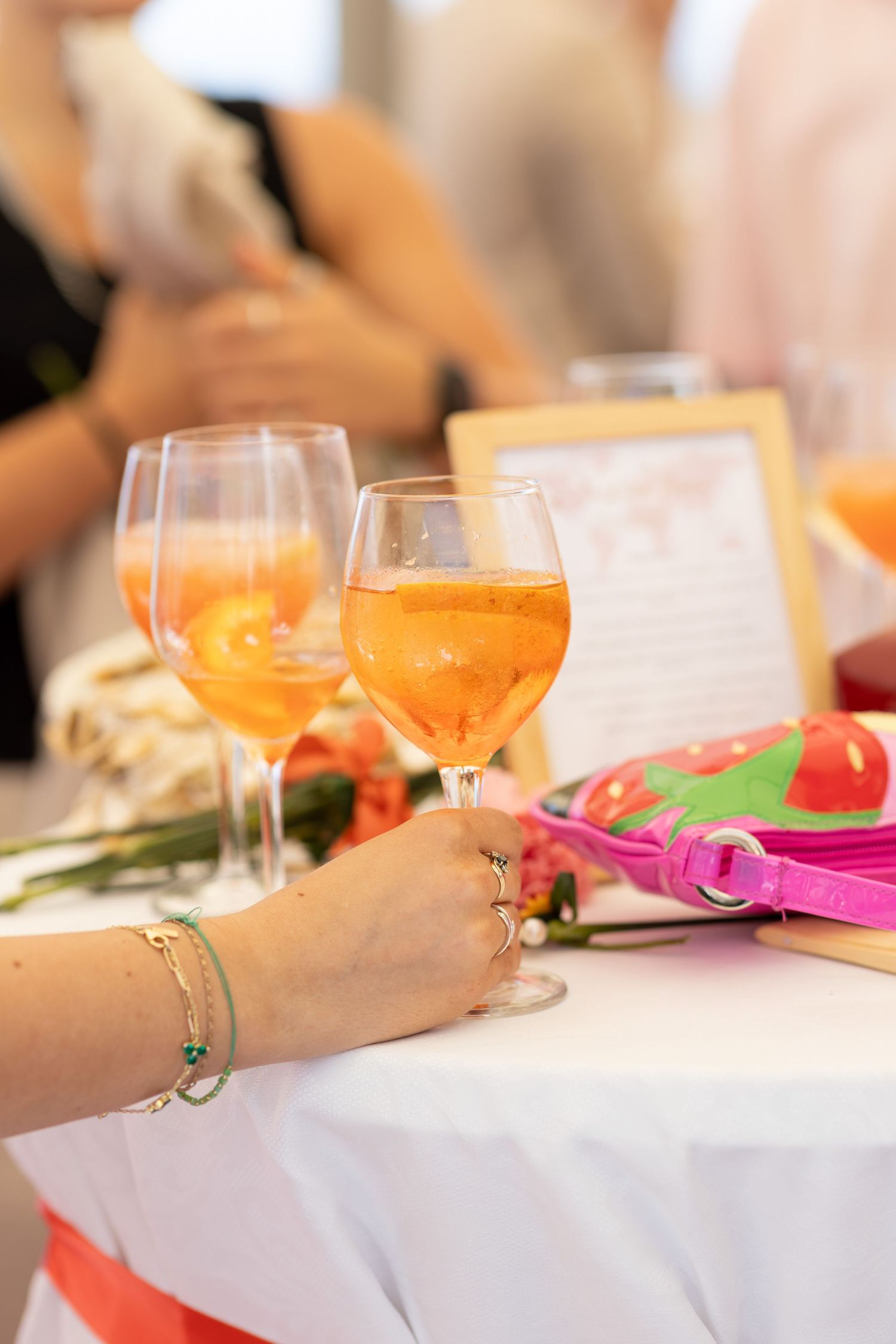 A hand holding a glass of Aperol Spritz at an elegant party table with flowers and decorations.