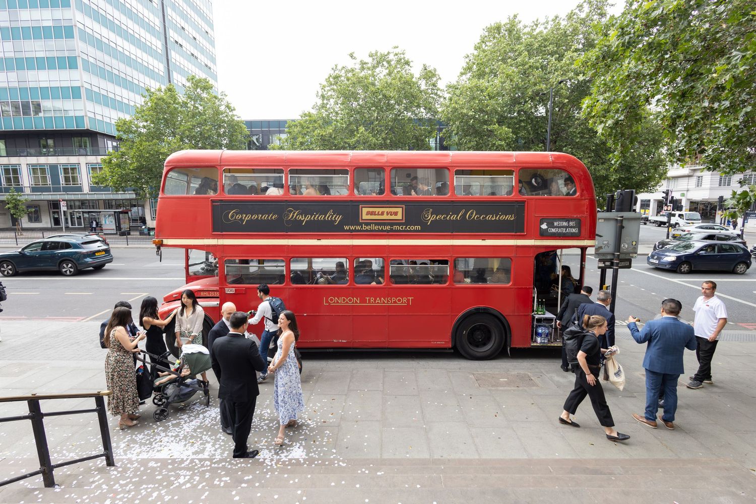 Wedding guests boarding classic red London double-decker bus for wedding transportation.
