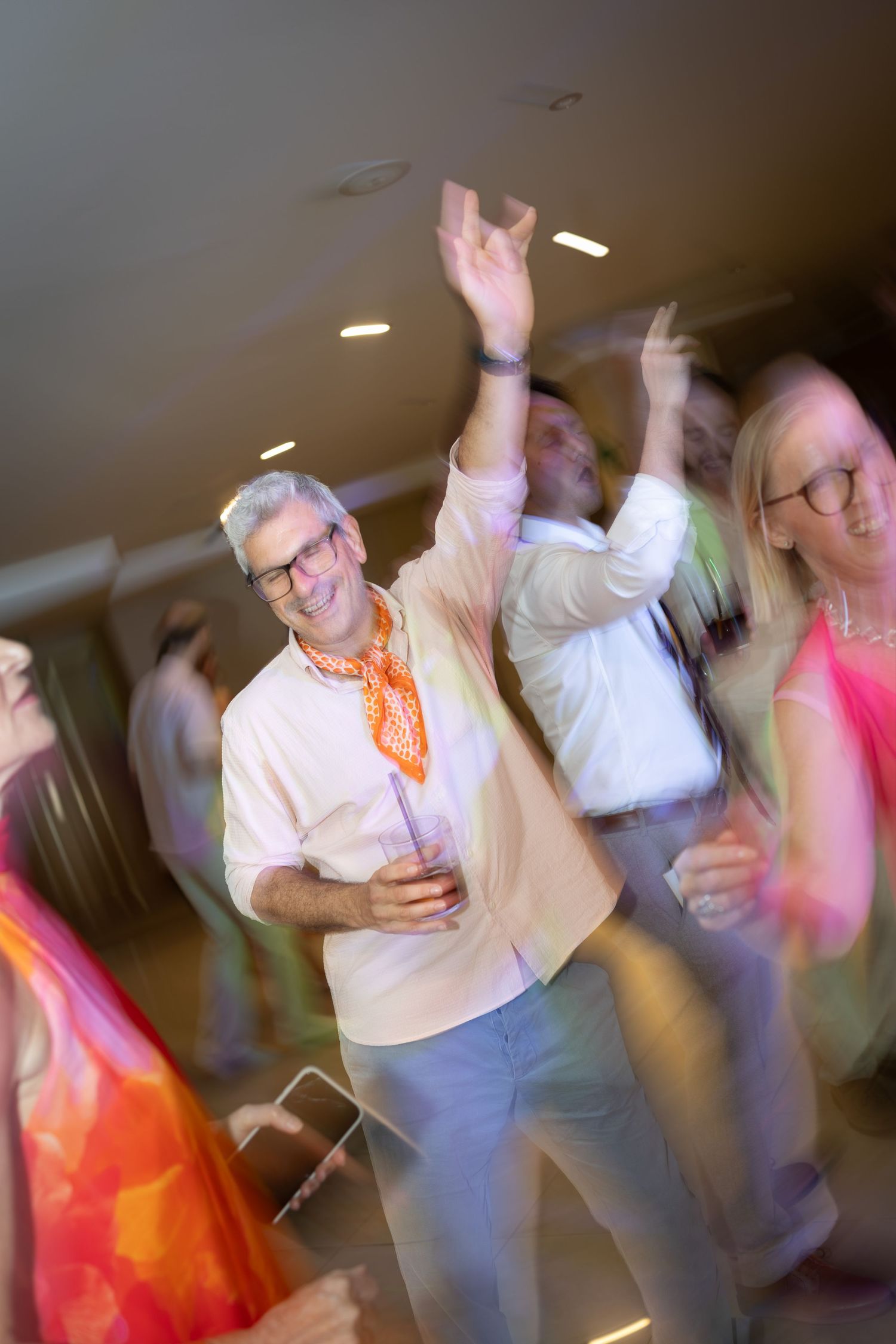 Motion-blurred photo of smiling guests dancing energetically at a lively wedding reception party.