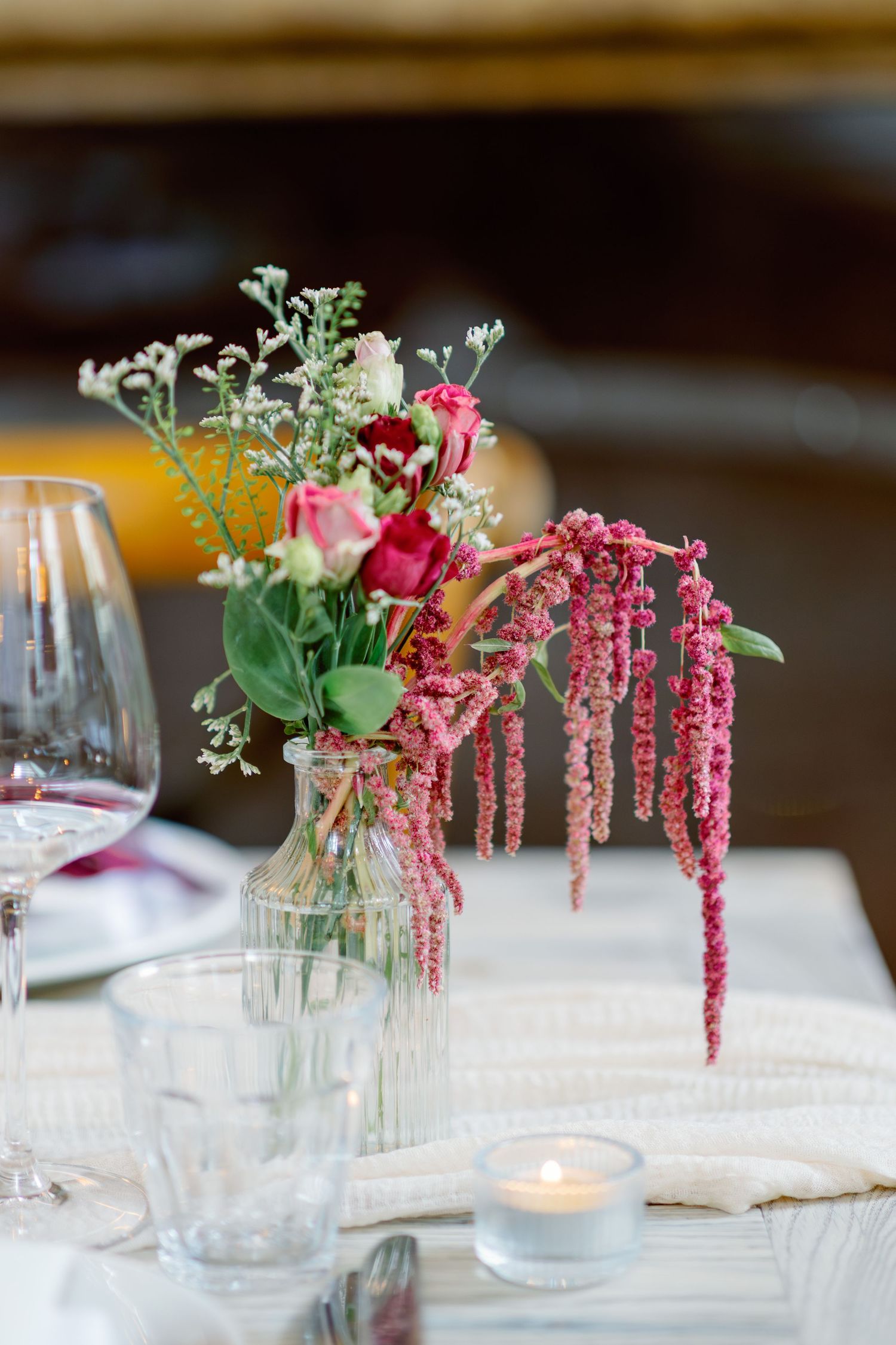 Elegant wedding table centerpiece with pink and burgundy flowers in glass vase with candle.