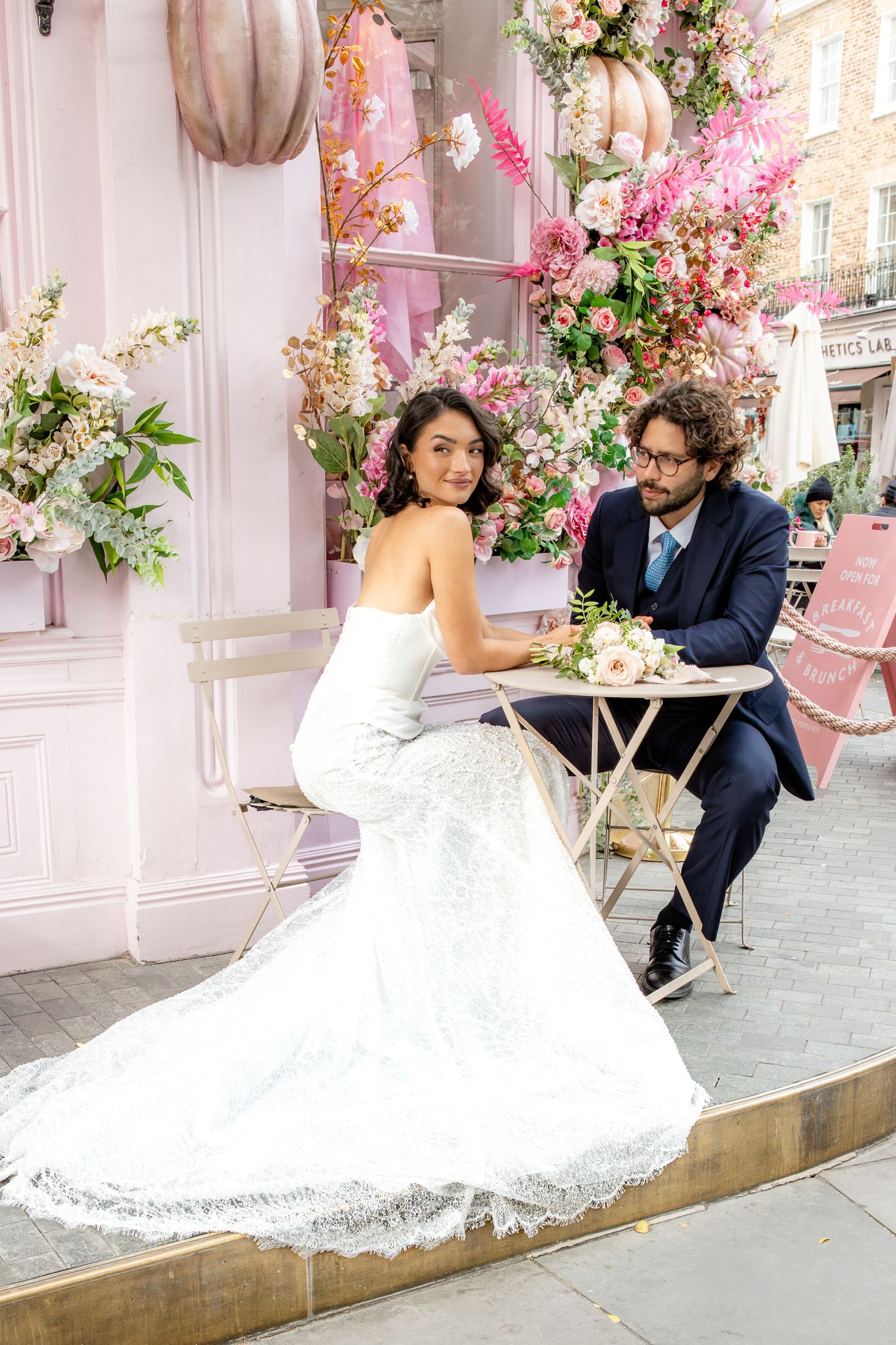 Romantic wedding scene with floral decorations and white dress against pink-tinted backdrop.