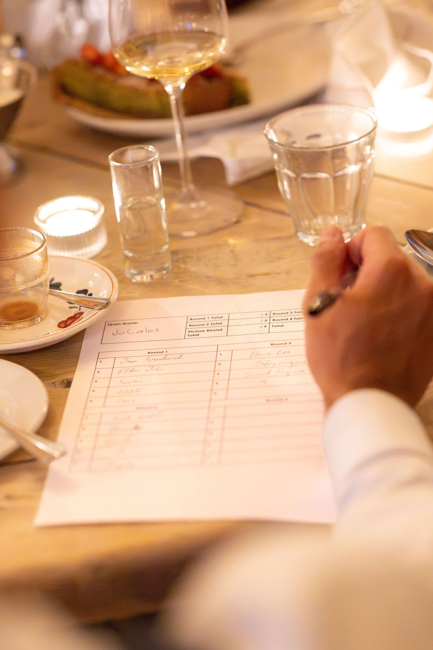 Guest filling out wedding menu card at candlelit reception table with wine glasses and plates.