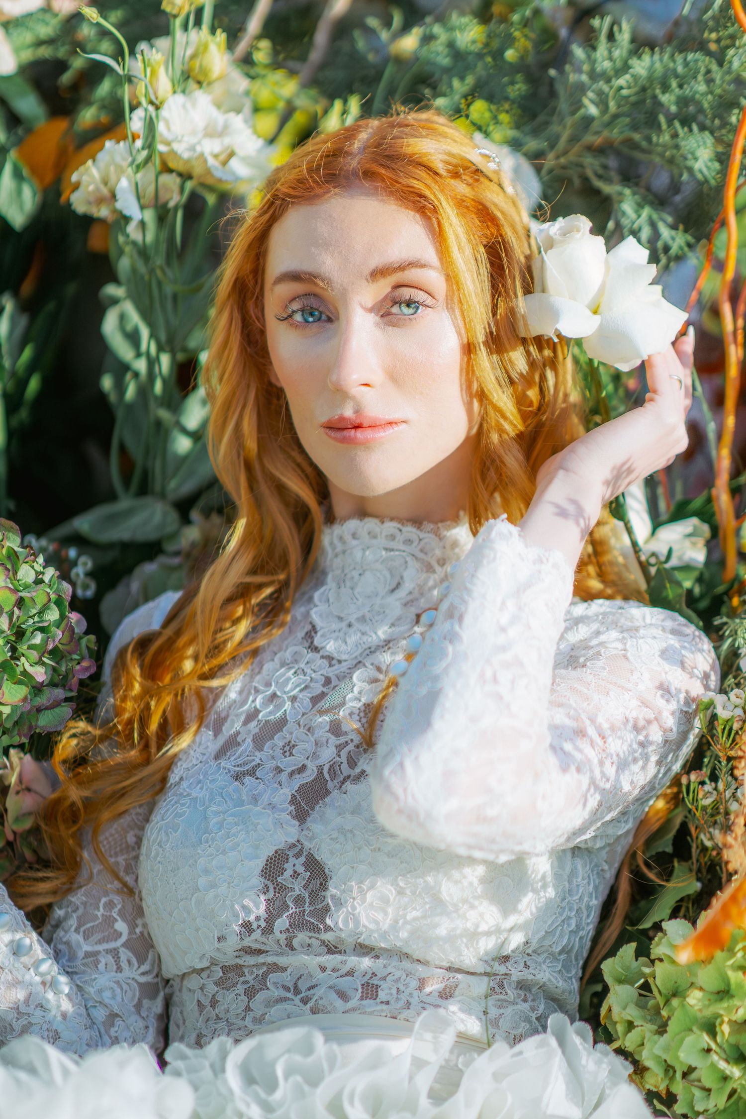 Ethereal bridal portrait with white lace dress amidst garden greenery and flowers.