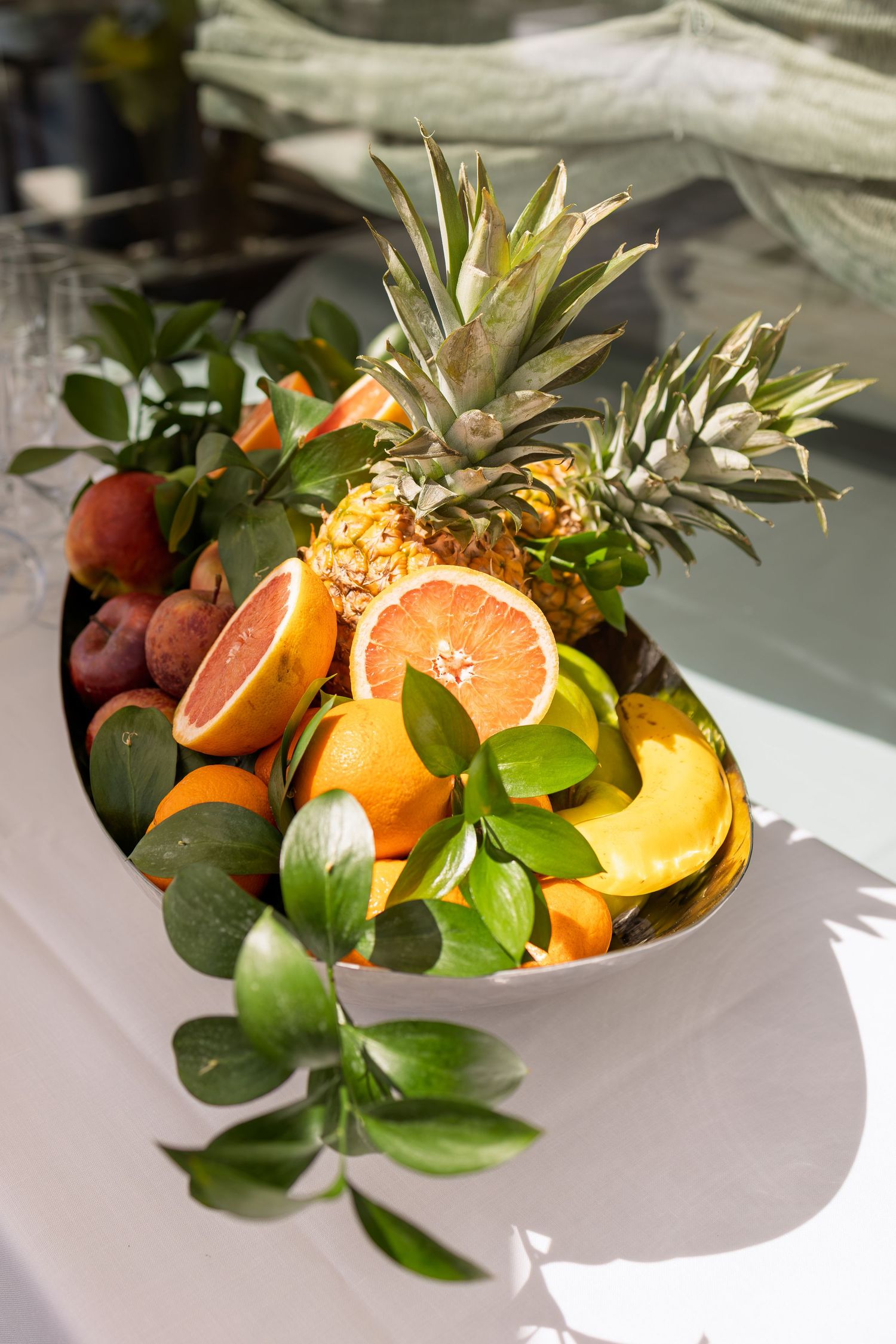 Elegant fruit display bowl with pineapple, oranges, grapefruit, and tropical fruits on a white table.