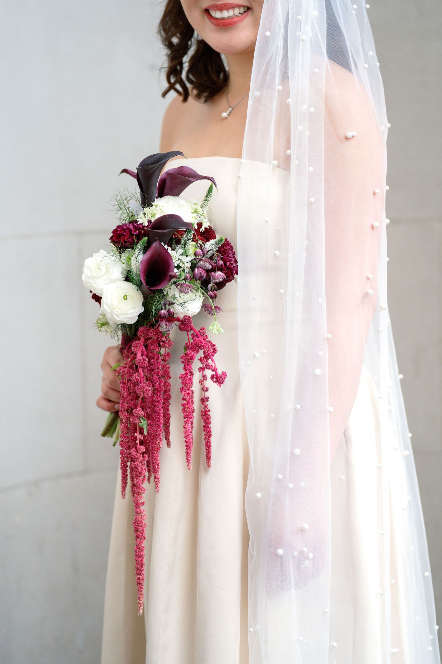 Smiling bride in white strapless gown holds a cascading burgundy and white wedding bouquet.