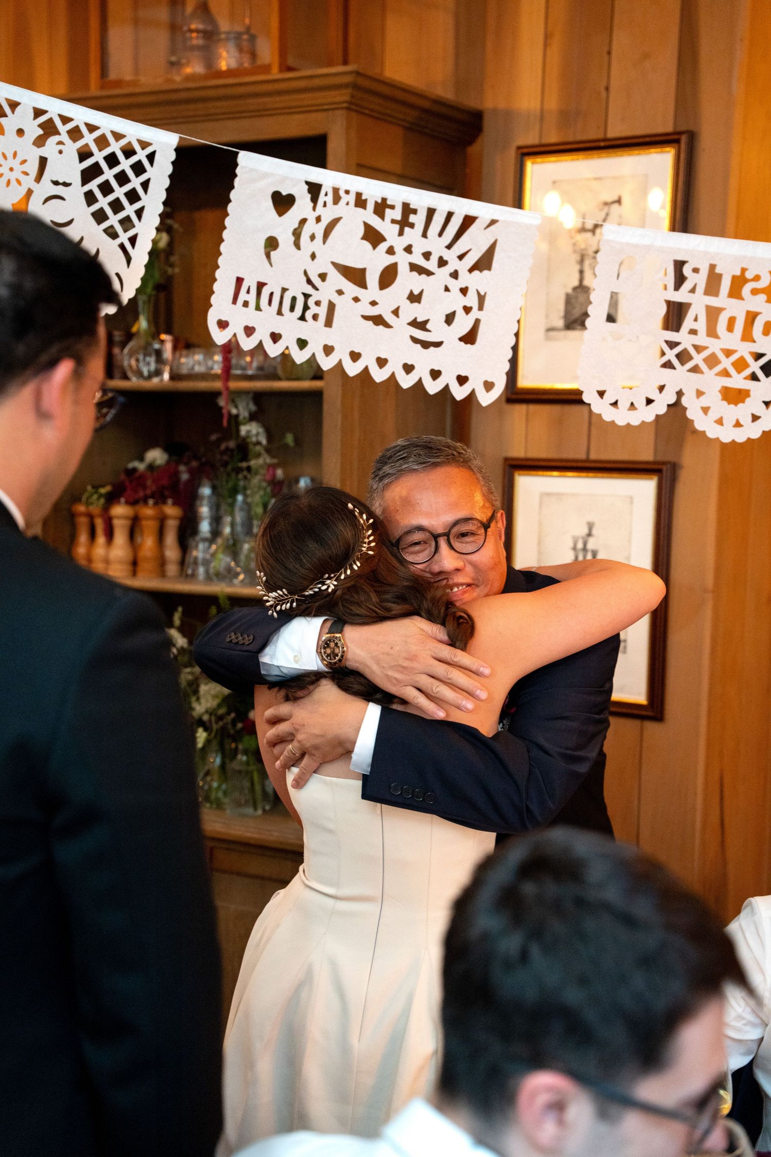 Bride embraces wedding guest warmly at reception decorated with papel picado banners.