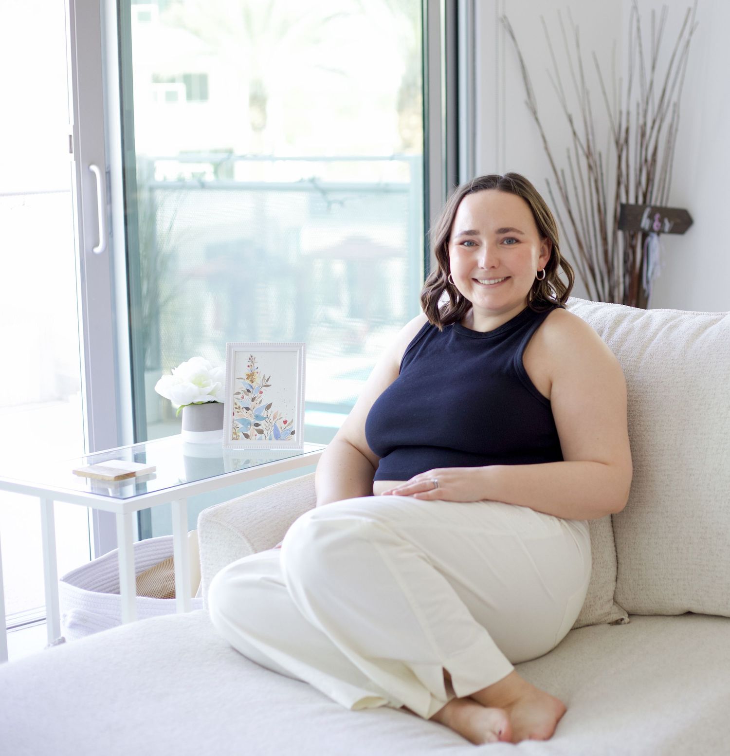 Person relaxing on white couch in bright, modern room with large windows.
