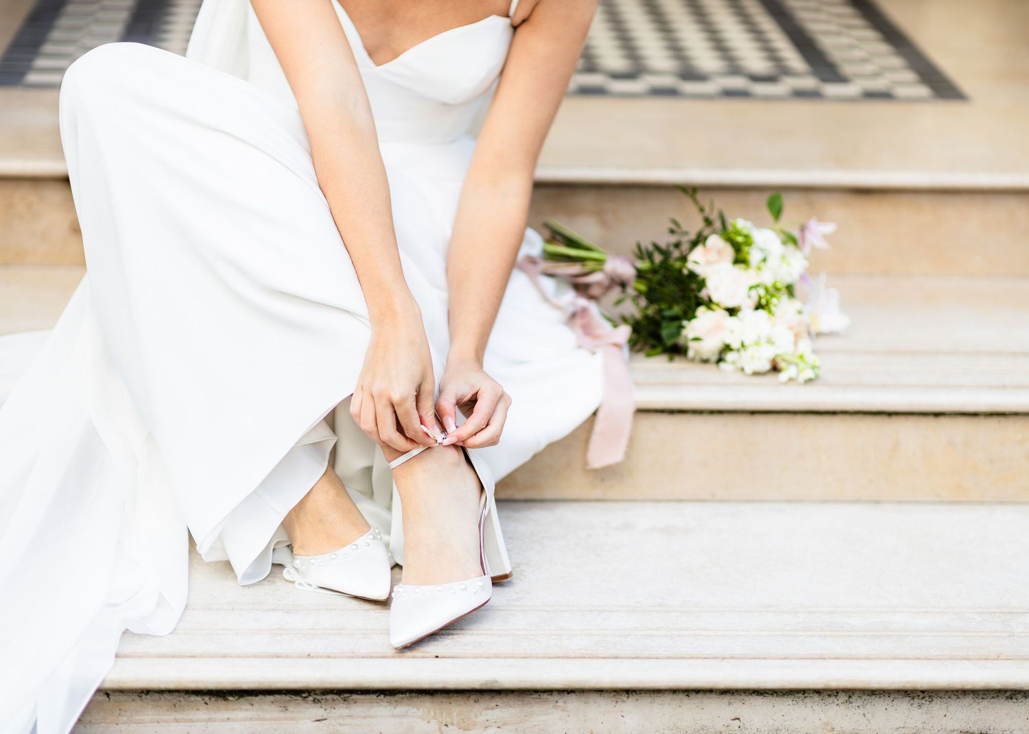 Close-up details of bridal shoes and dress hem on stone steps.