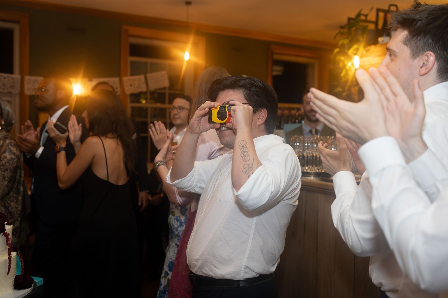 Guest uses a novelty camera toy while others clap and dance at a lively wedding reception party.
