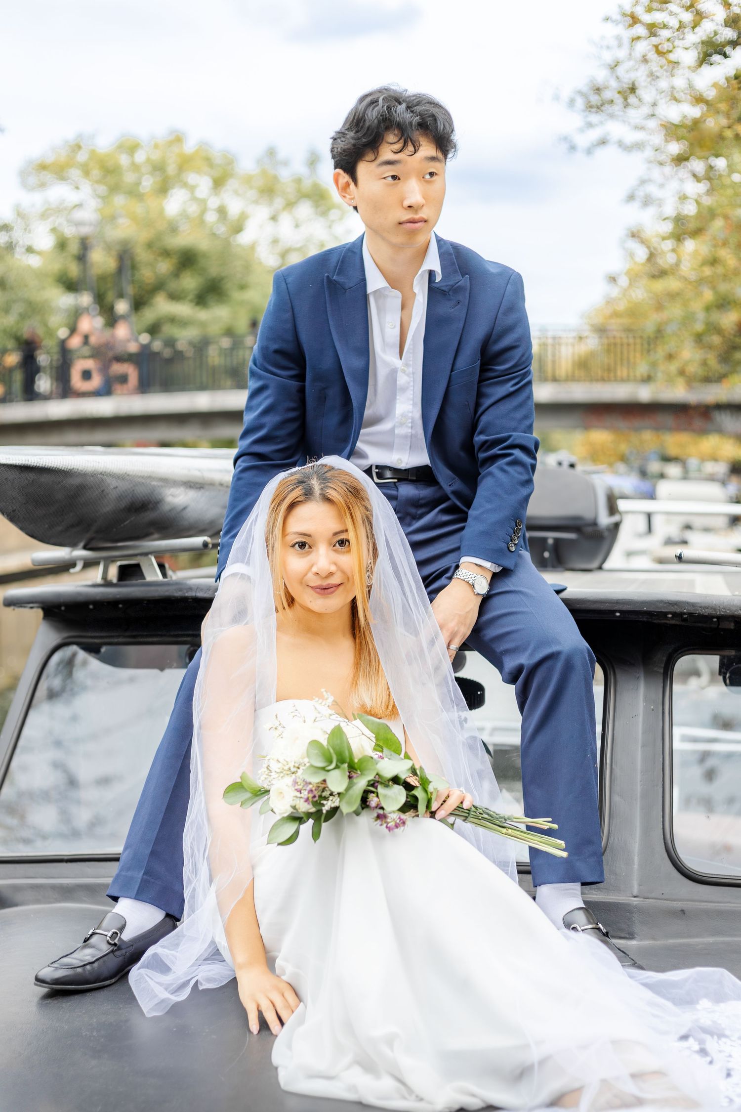 Wedding couple poses casually on vintage black car during outdoor photoshoot.