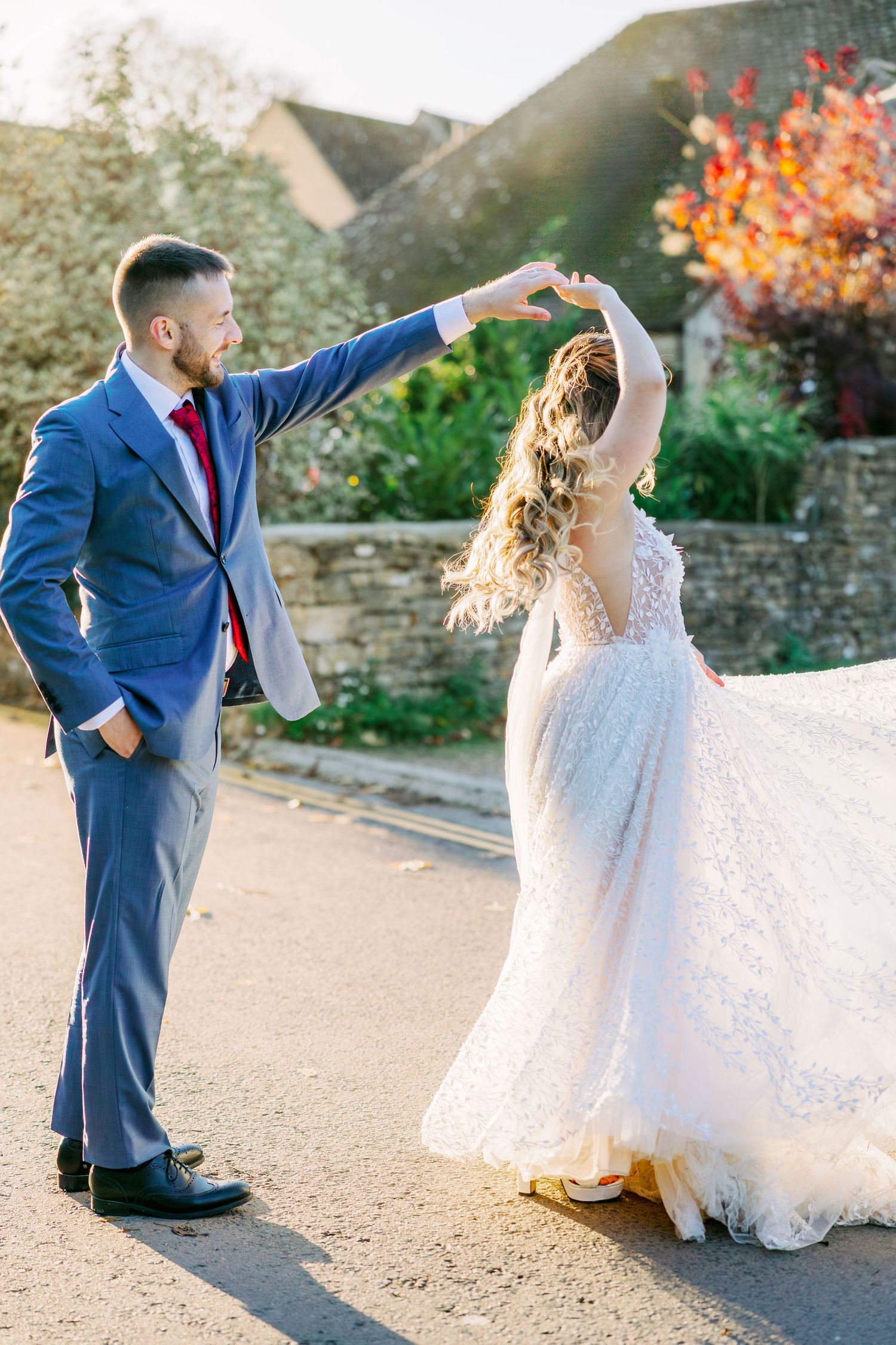 Bride and groom in blue suit dance together on a garden path.