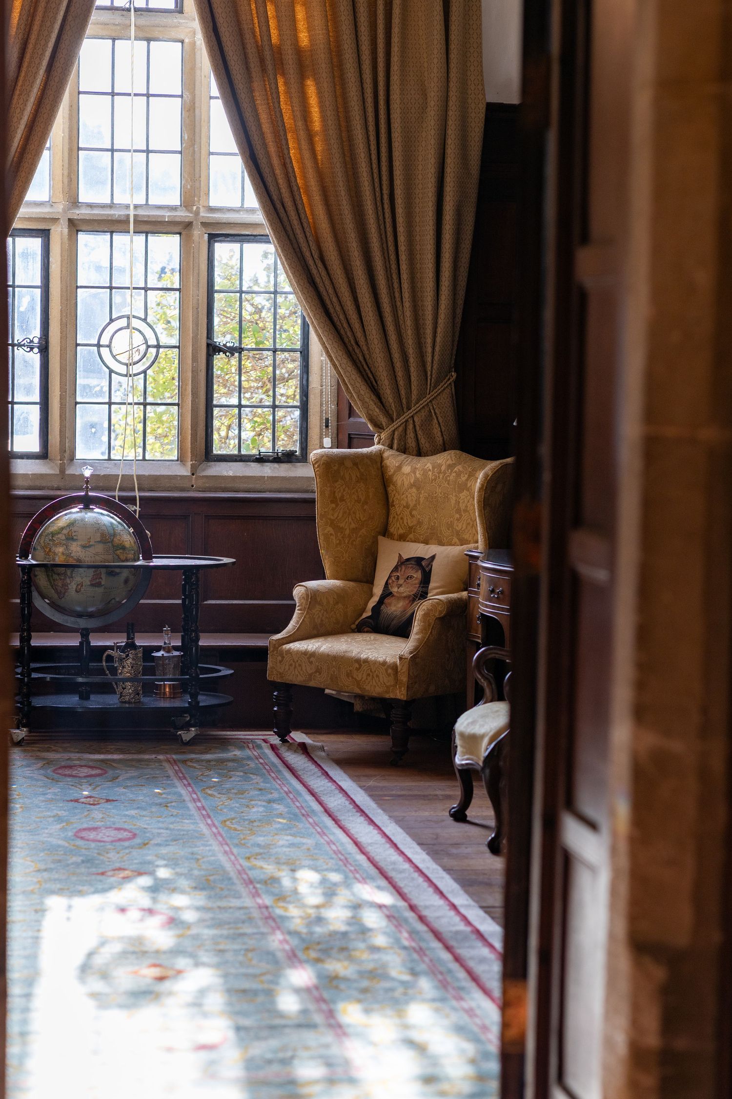 Elegant historic room with tall windows, brown curtains, and patterned carpet in warm natural lighting.