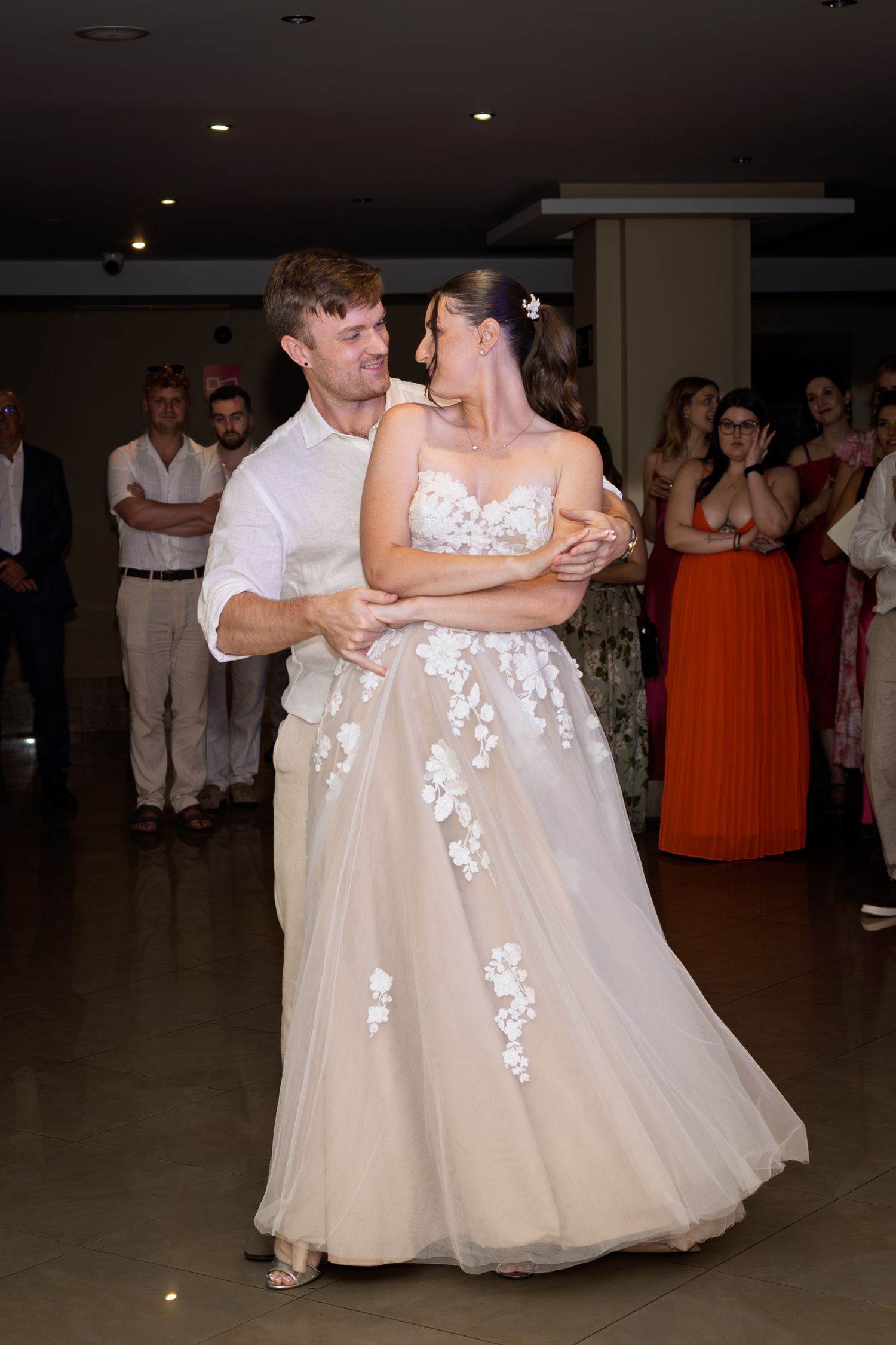 A bride and groom share their first dance surrounded by guests at their wedding reception.