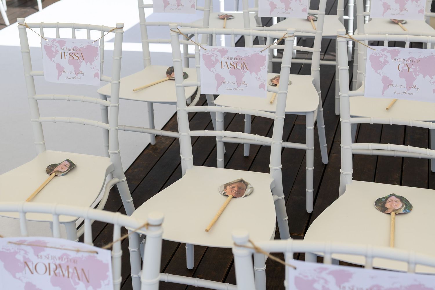 White Chiavari chairs decorated with personalized fan programs and pink signage for an outdoor wedding ceremony.