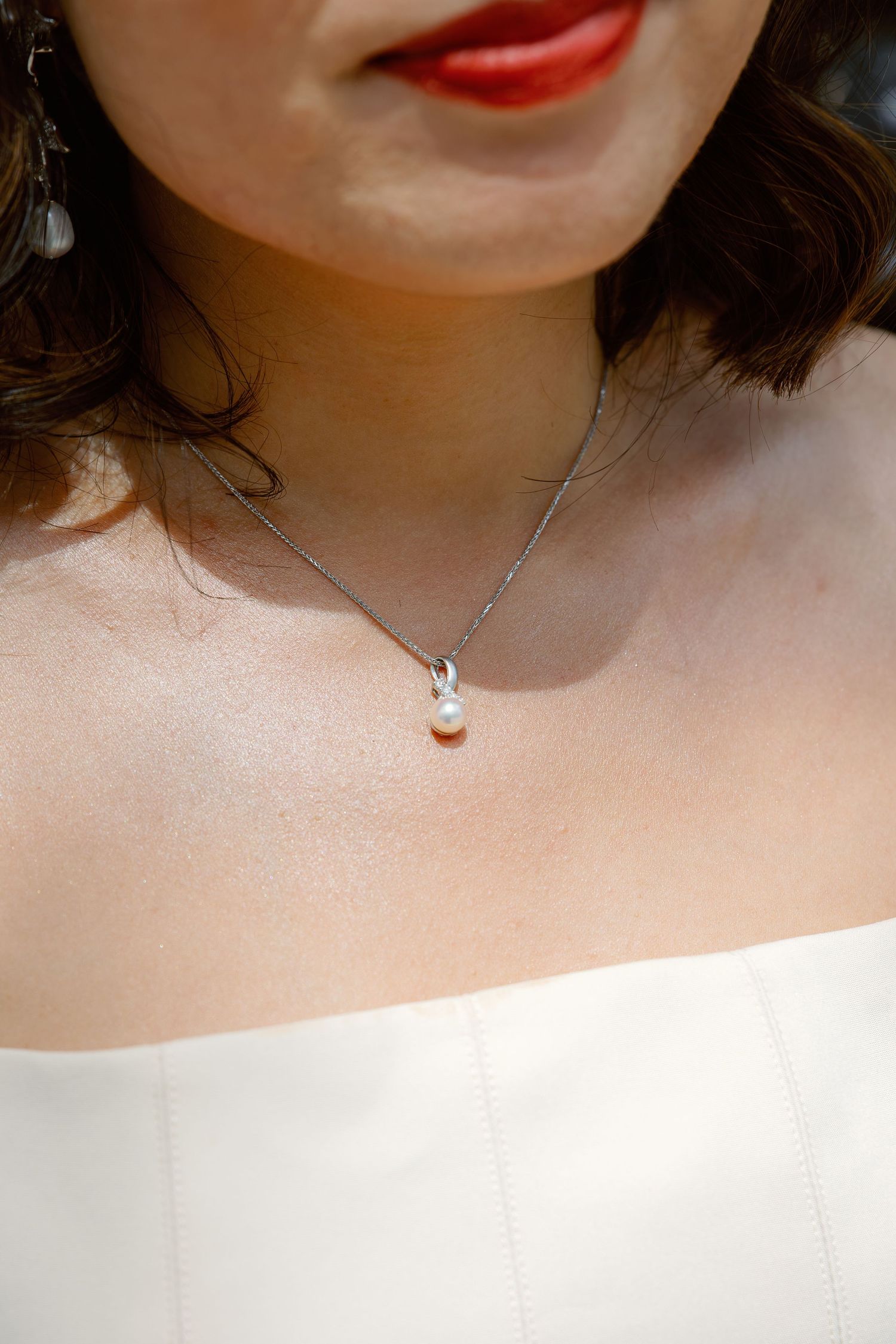 Close-up of bride wearing a delicate pearl pendant necklace and strapless white gown.