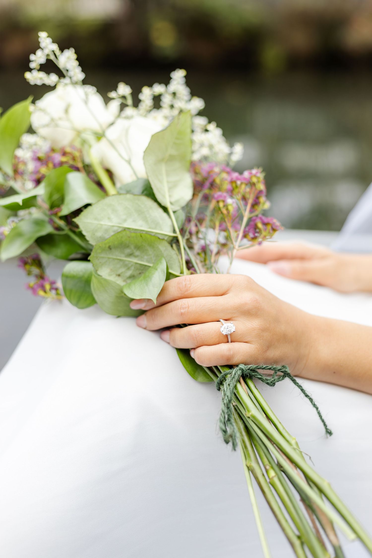 Detail shot of hands holding delicate white and green wedding bouquet.