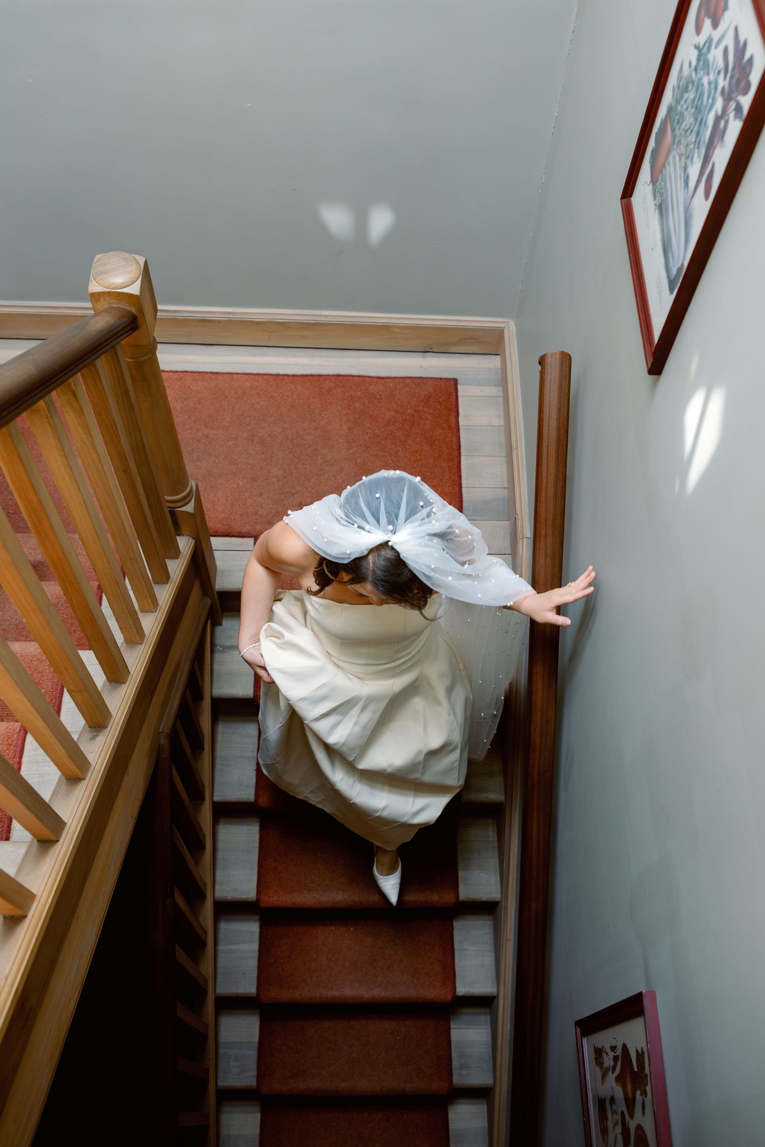 Bride in white wedding dress descending wooden staircase viewed from above.