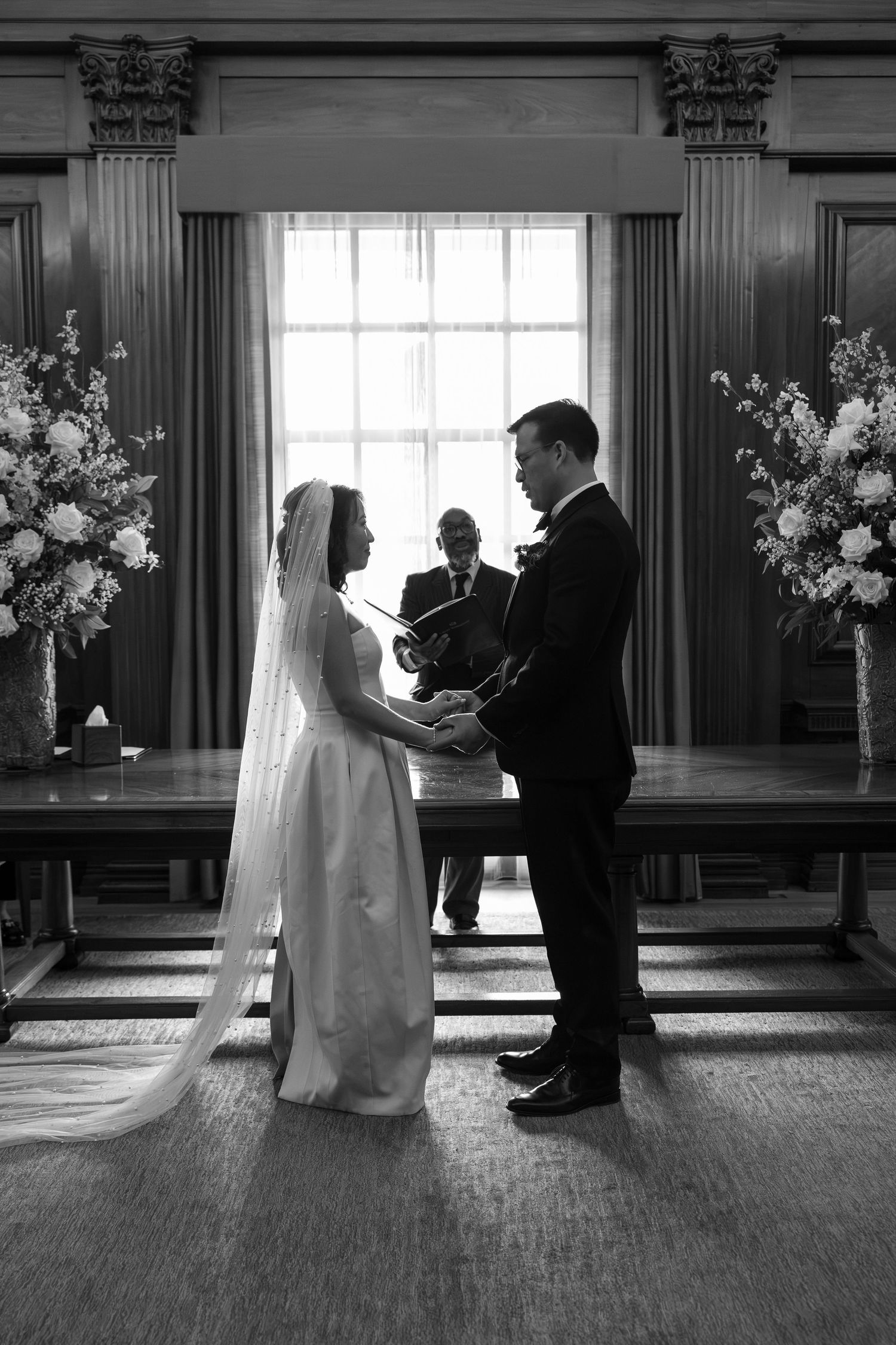 Black and white photo of bride and groom exchanging vows at altar.