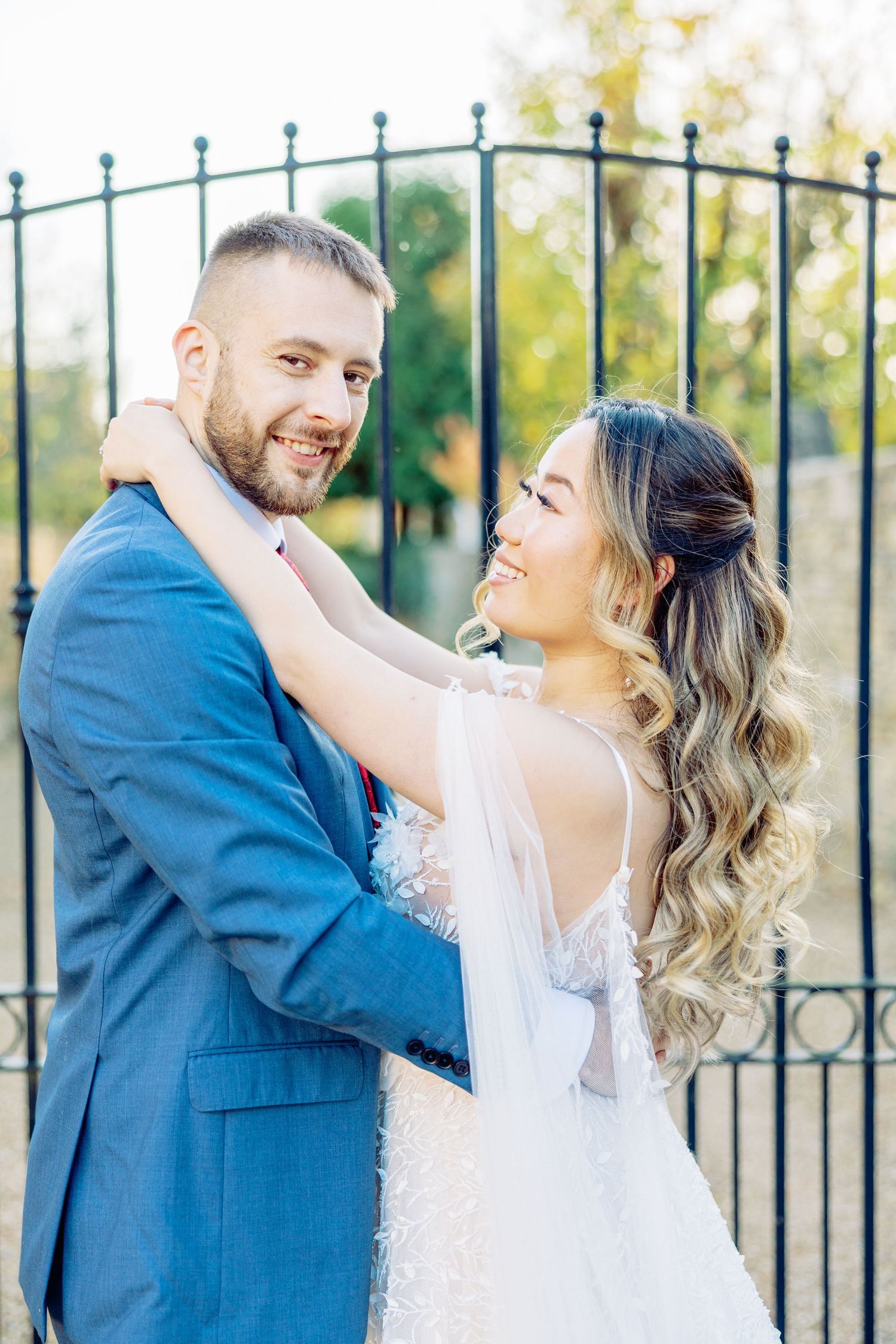 Newlyweds dancing and twirling by ornate iron gates outdoors.
