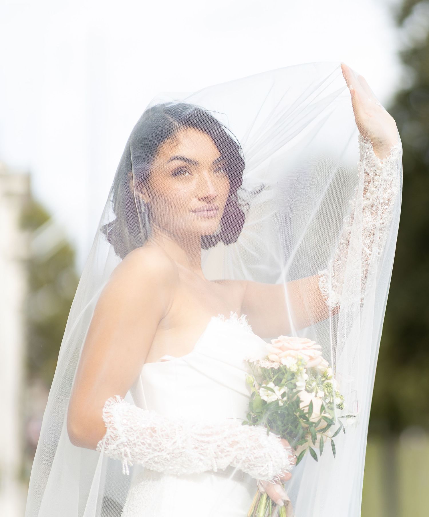 Ethereal bridal portrait through flowing white veil with delicate lace details.
