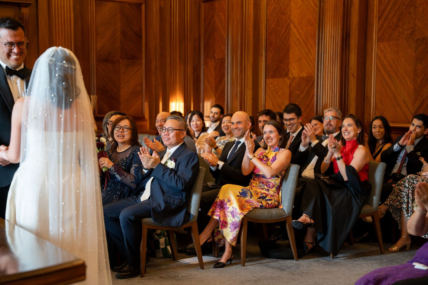 Wedding guests applauding and celebrating during an elegant indoor ceremony in a wood-paneled room.