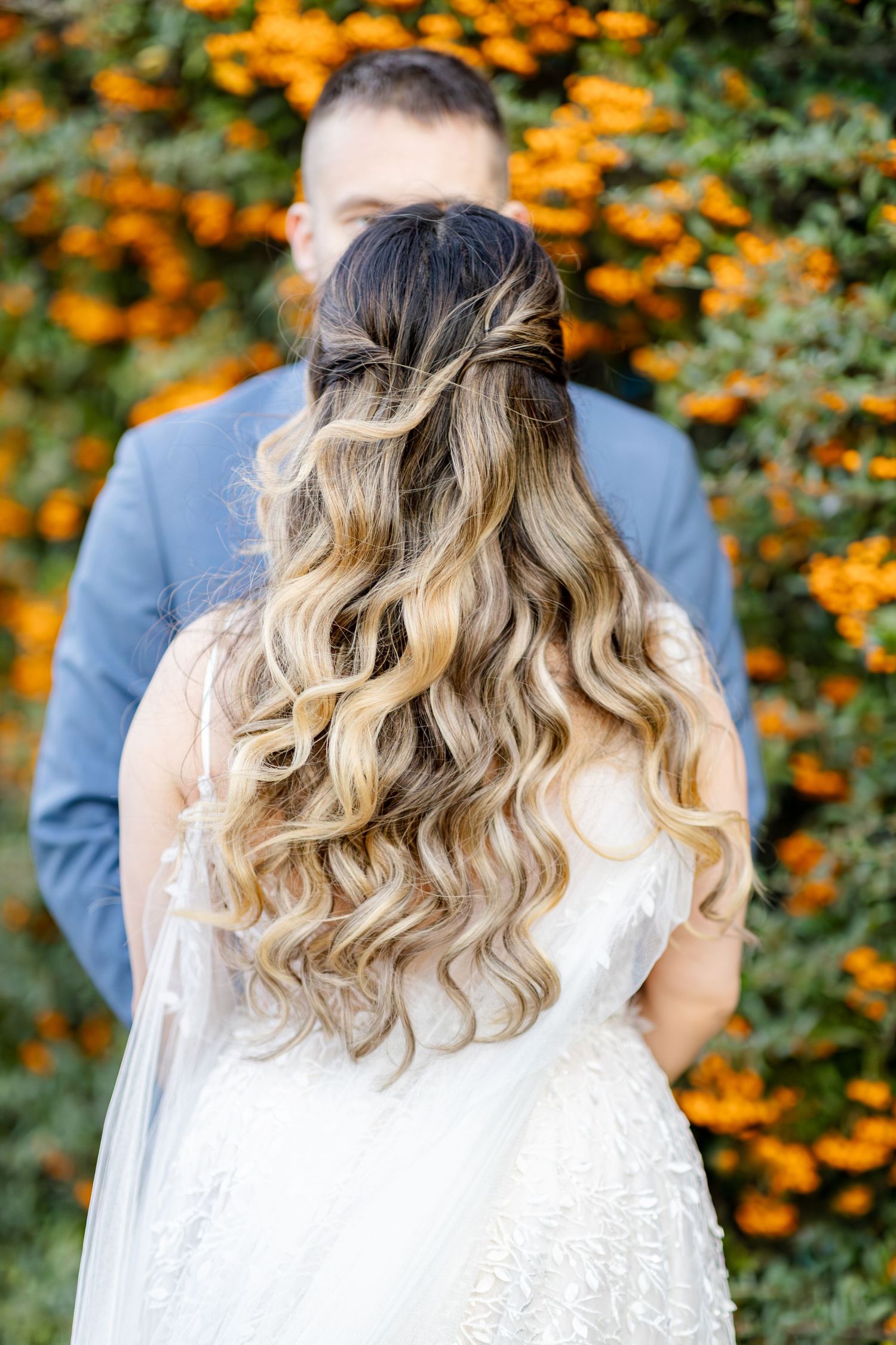 Close-up of bride's flowing blonde curls with orange flowers in background.