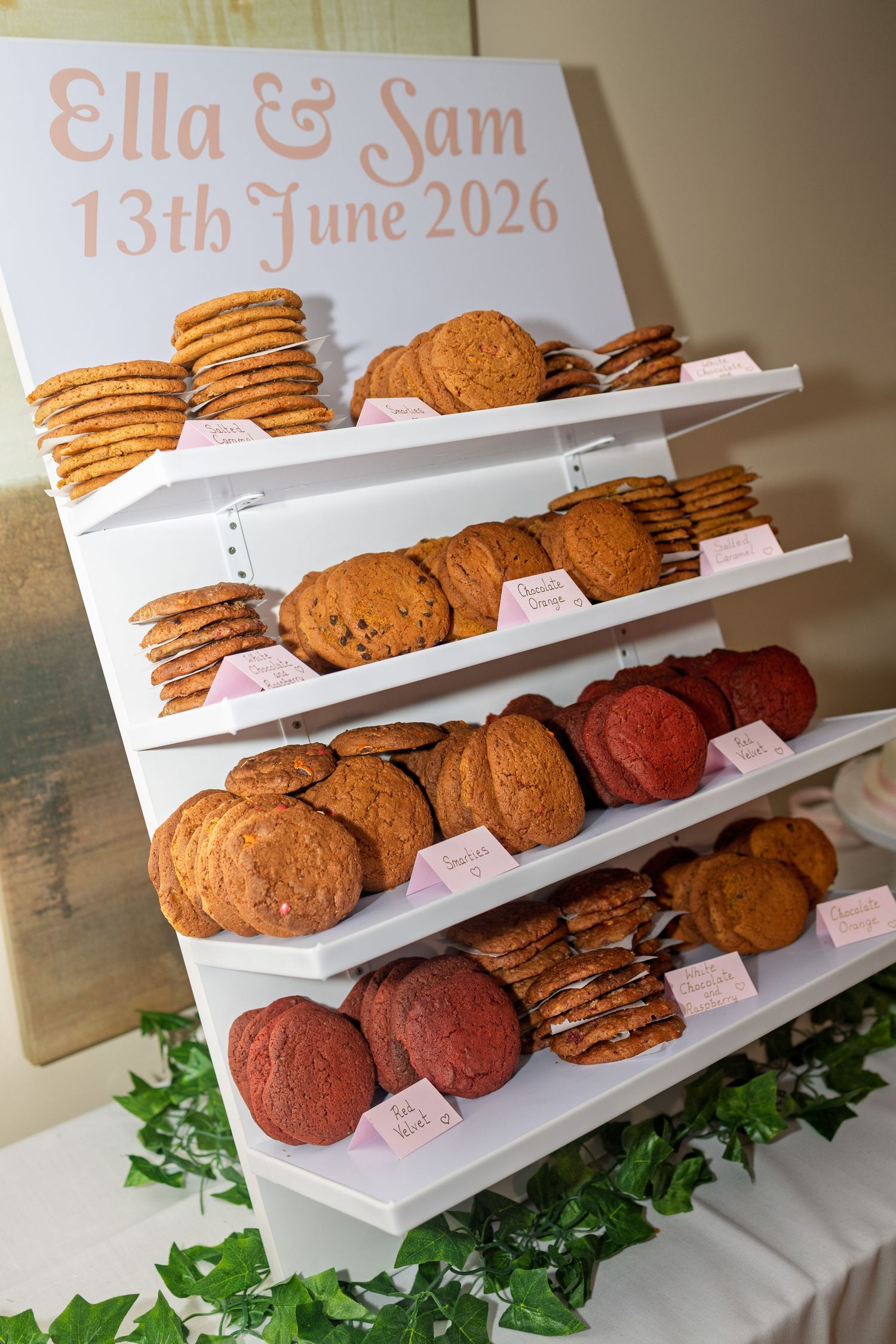 Wedding cookie display stand featuring assorted cookies with a personalized Ella and Sam 13th June 2026 sign.