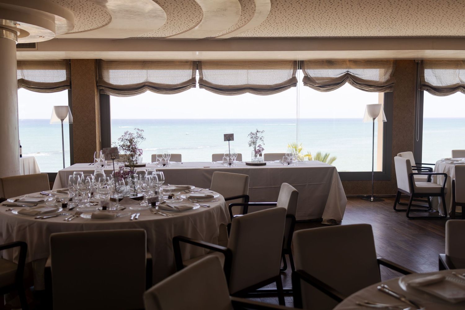 An elegant seaside wedding reception venue with round tables set with glassware and ocean views.