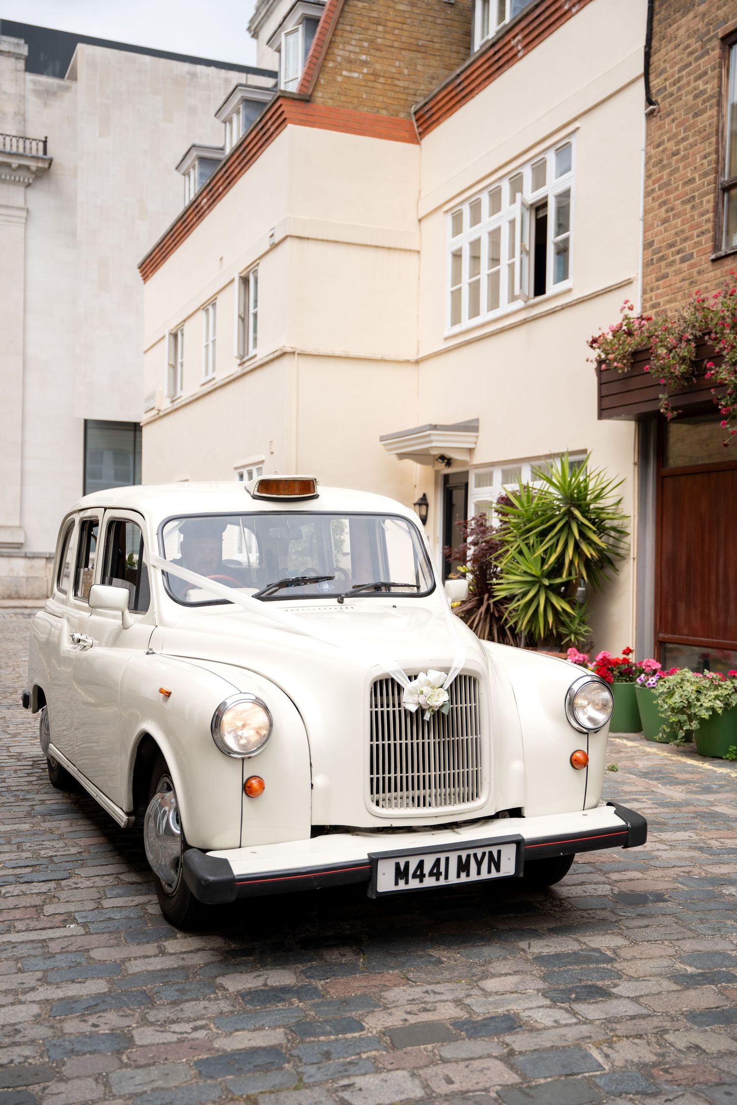 White vintage London taxi cab decorated with flowers parked on cobblestone mews street.