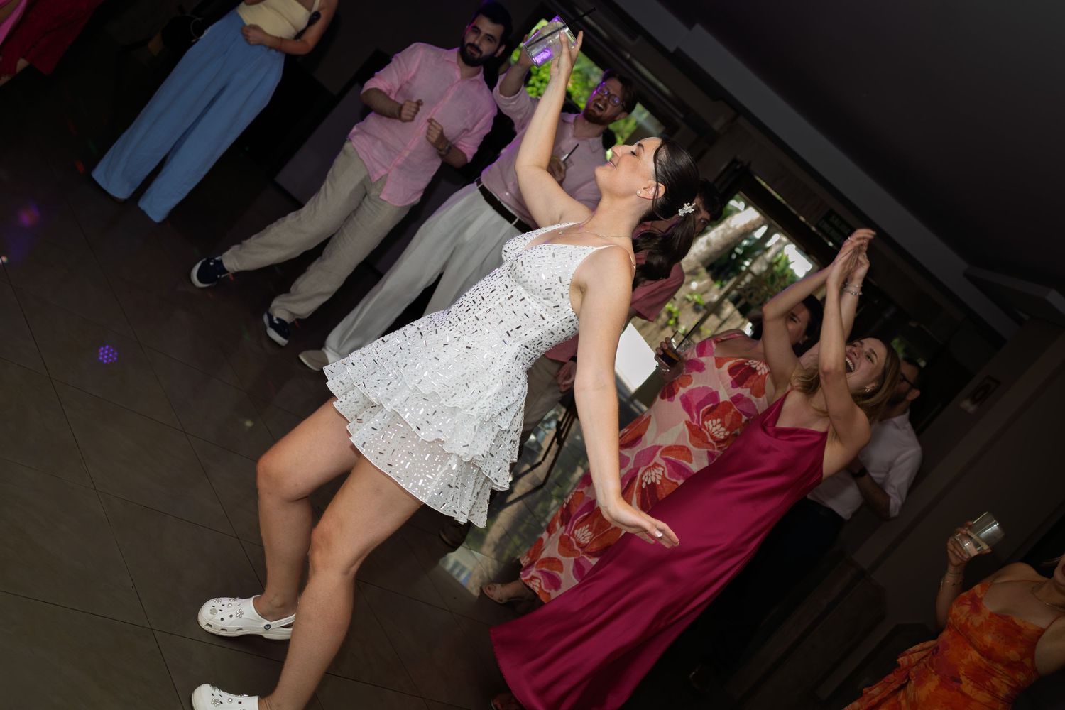 Bride in white dress tossing bouquet at wedding reception with guests in background.