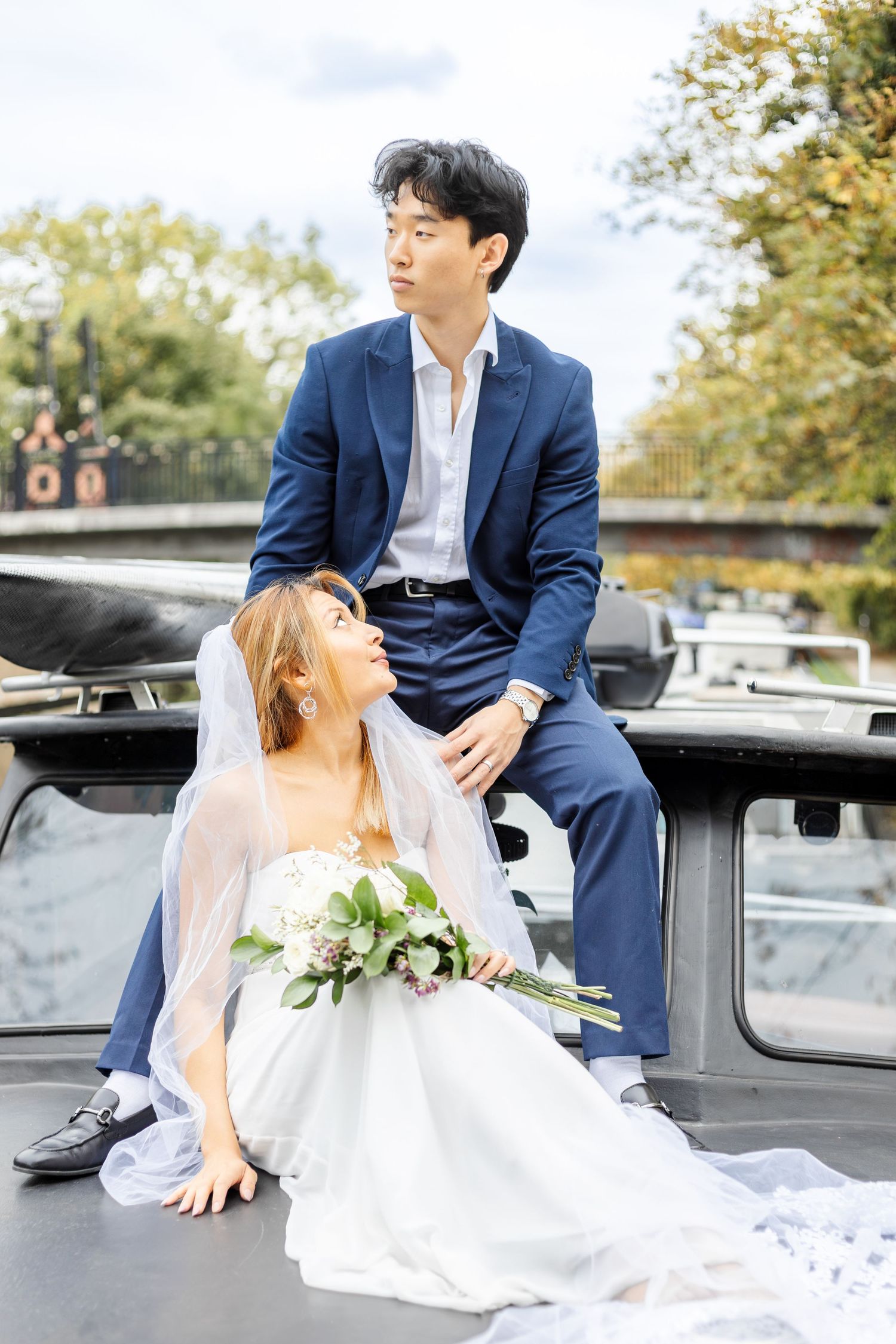 Newlyweds pose together on vintage car in outdoor autumn setting.
