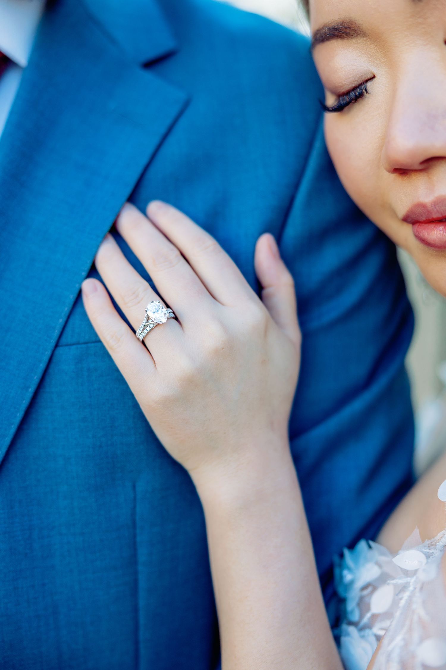 Close up detail of engagement ring on hand against blue suit jacket.