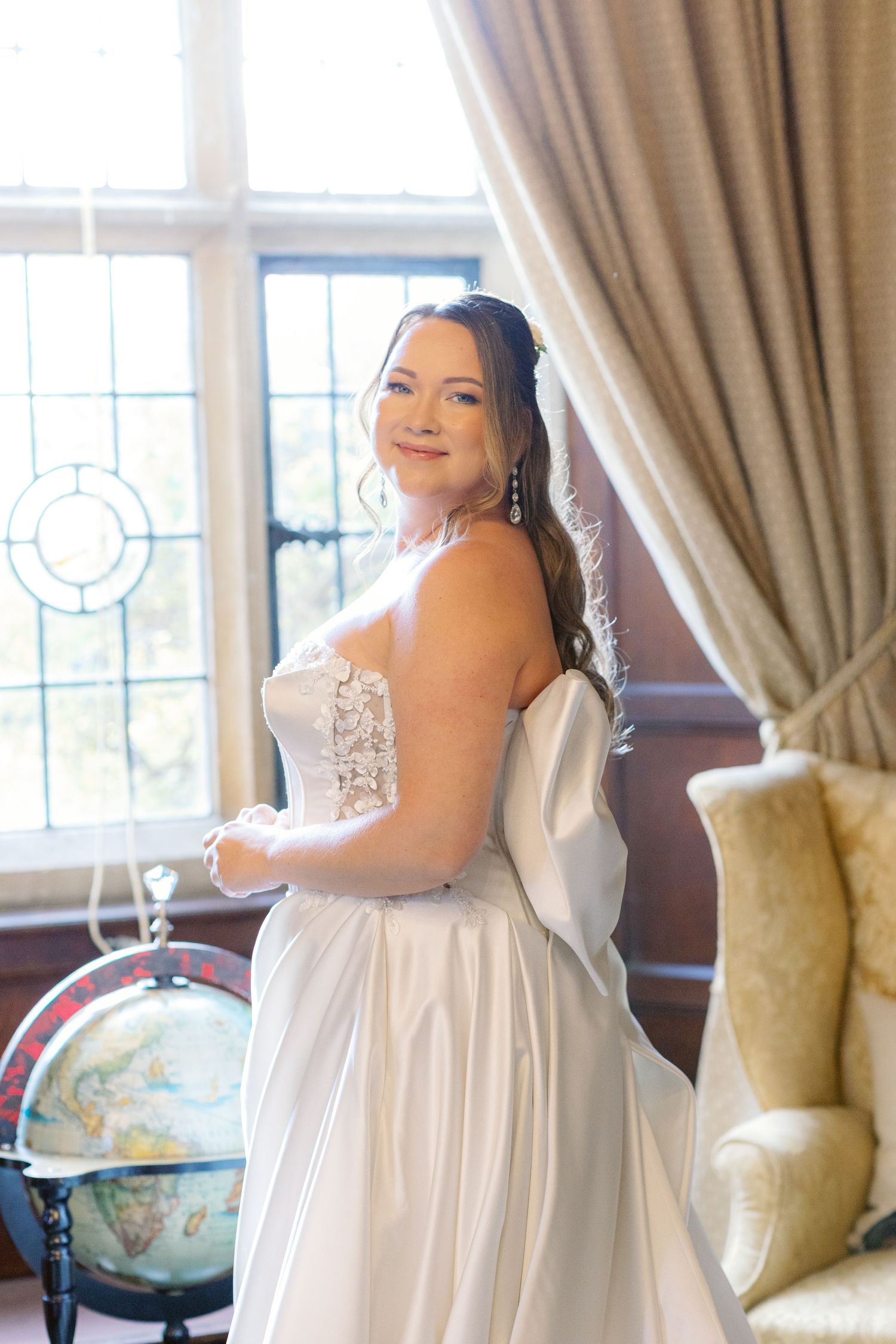 White formal dress photographed in an elegant room with curtains and a globe decor.