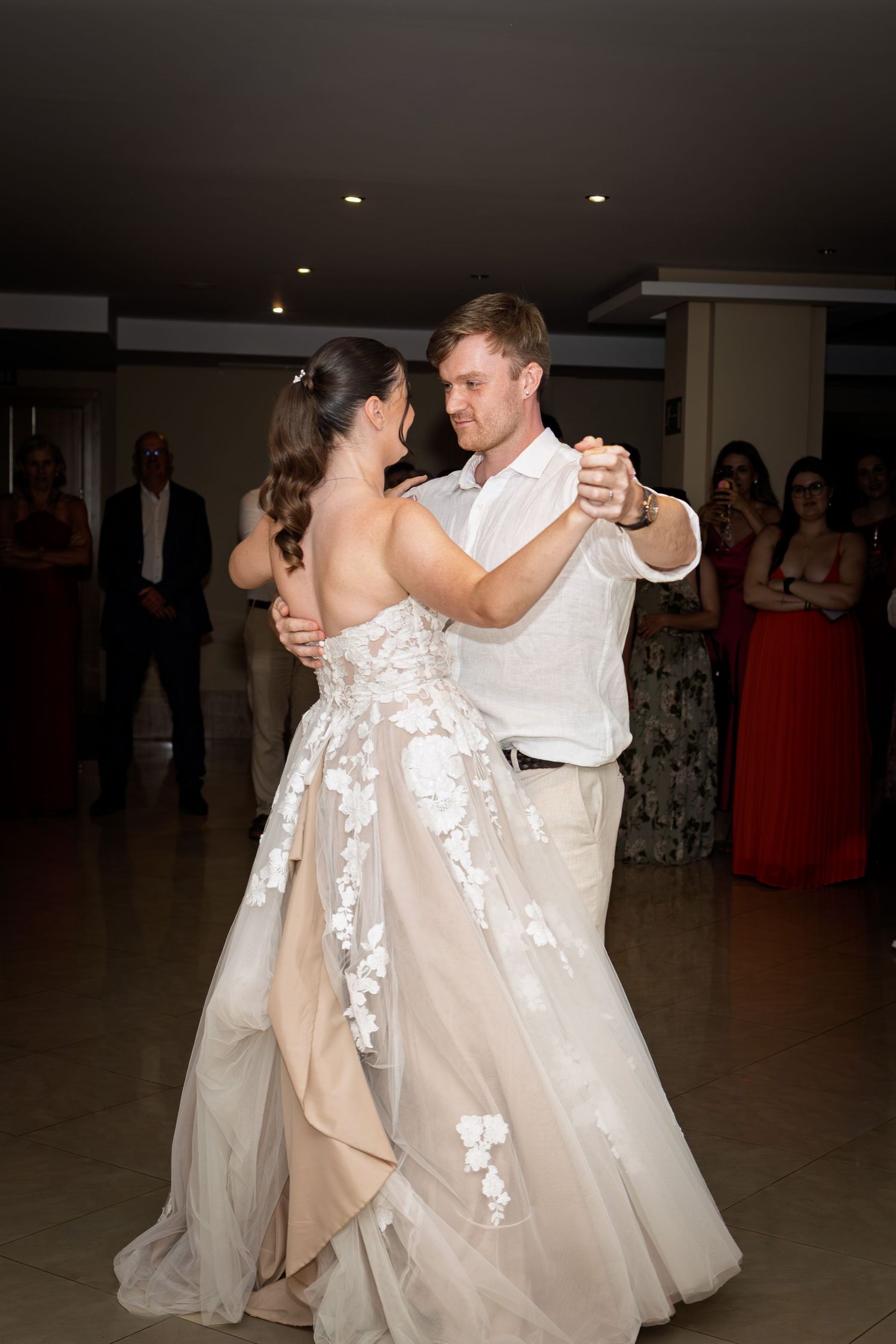 A couple shares an elegant first dance in a ballroom as wedding guests watch in the background.