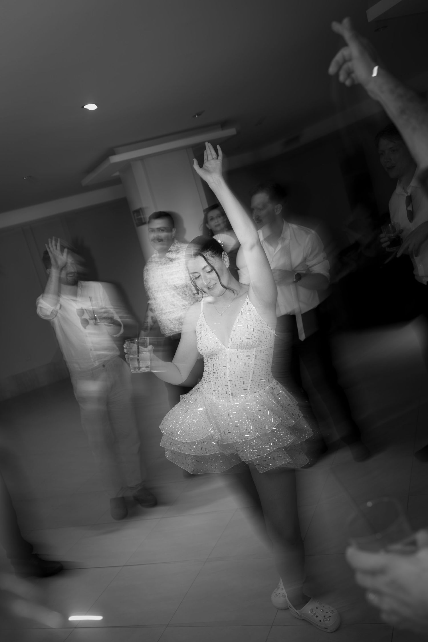 Black and white motion blur photo of bride dancing with raised arms at wedding reception party.