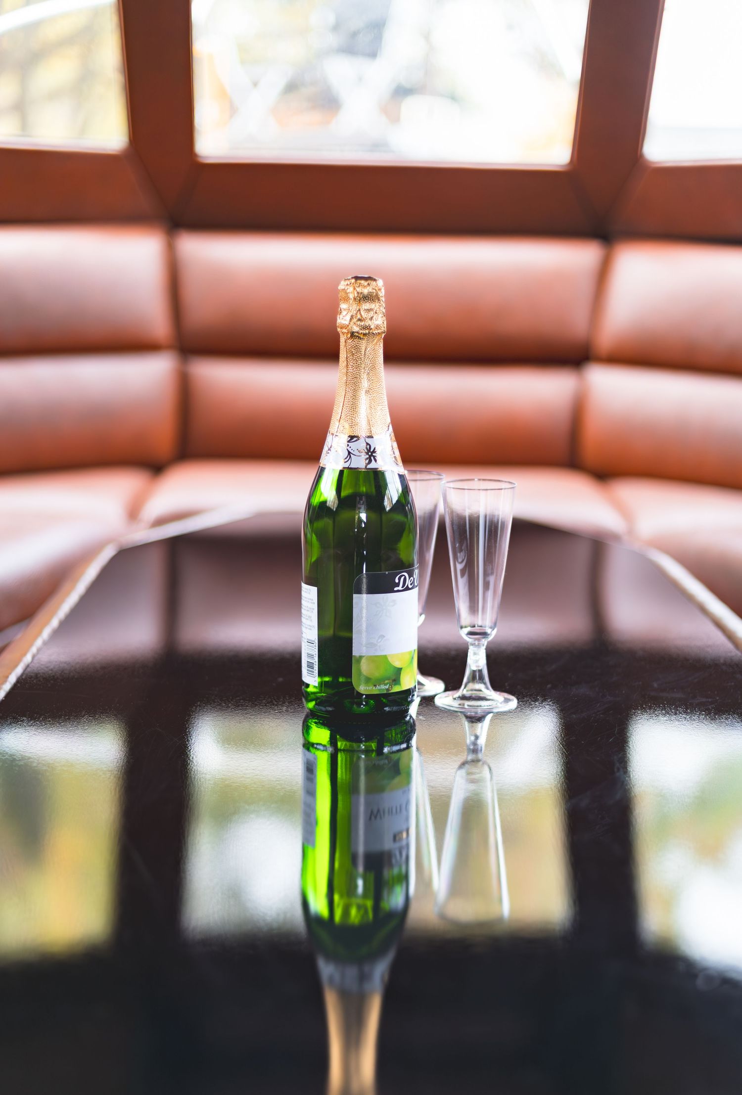 Green wine bottles and empty martini glasses sit on a dark table against brown leather booth seating.