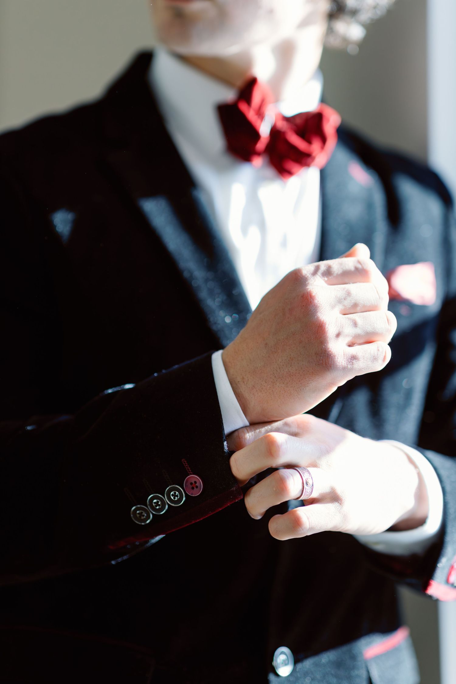 Close-up shots of hands adjusting formal black suit jacket and red bowtie.