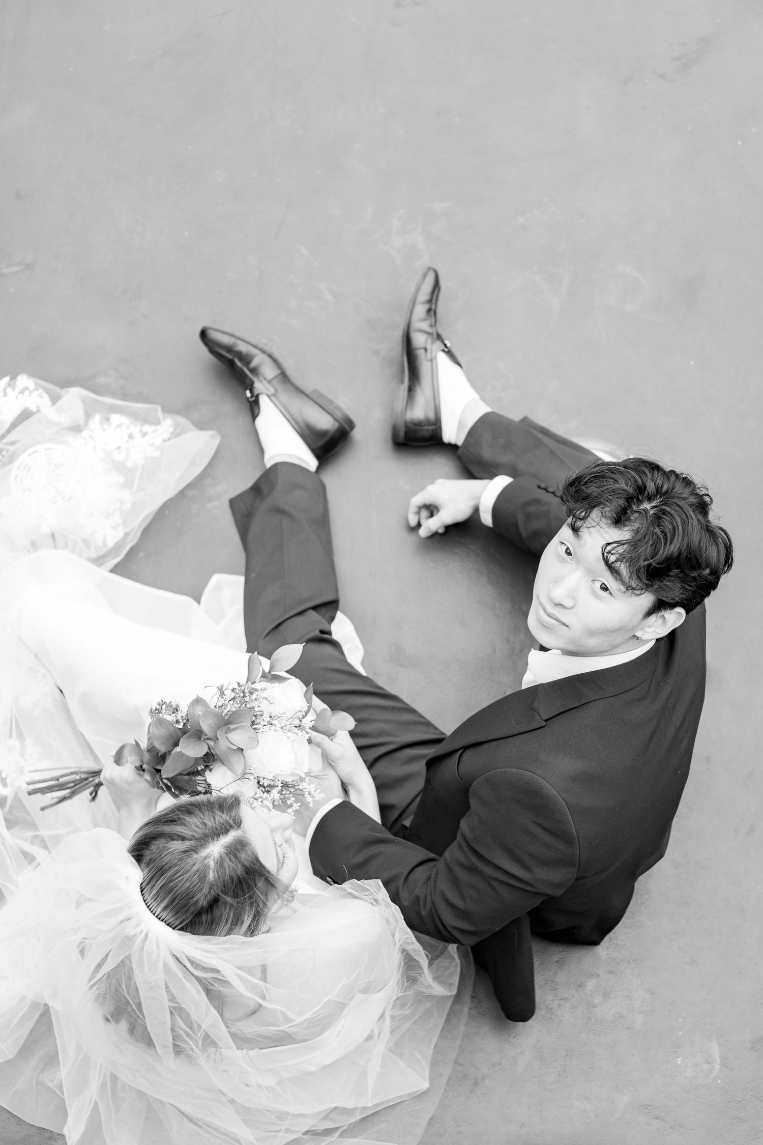 Black and white wedding photos show couple lying on ground in elegant formal attire.