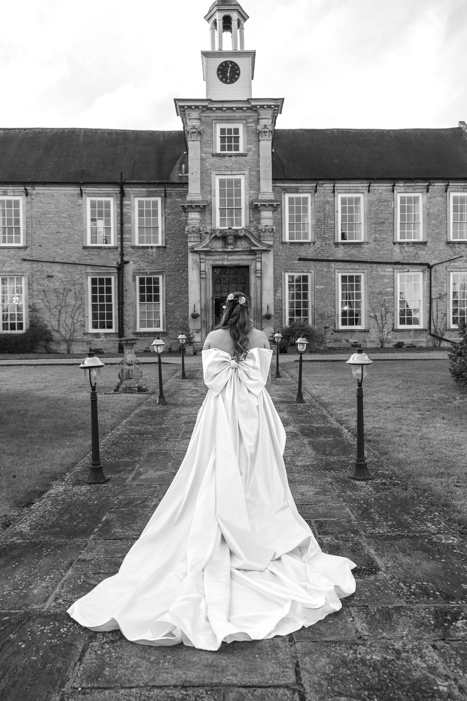 Black and white photo of bride in flowing gown facing historic clock tower building.