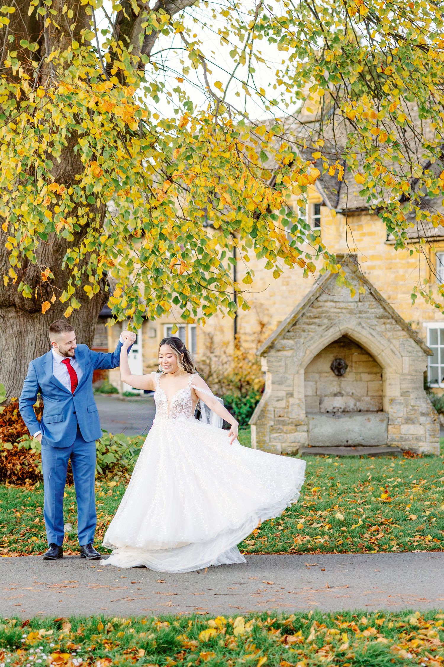 Playful wedding portraits in front of a stone church with fallen autumn leaves.