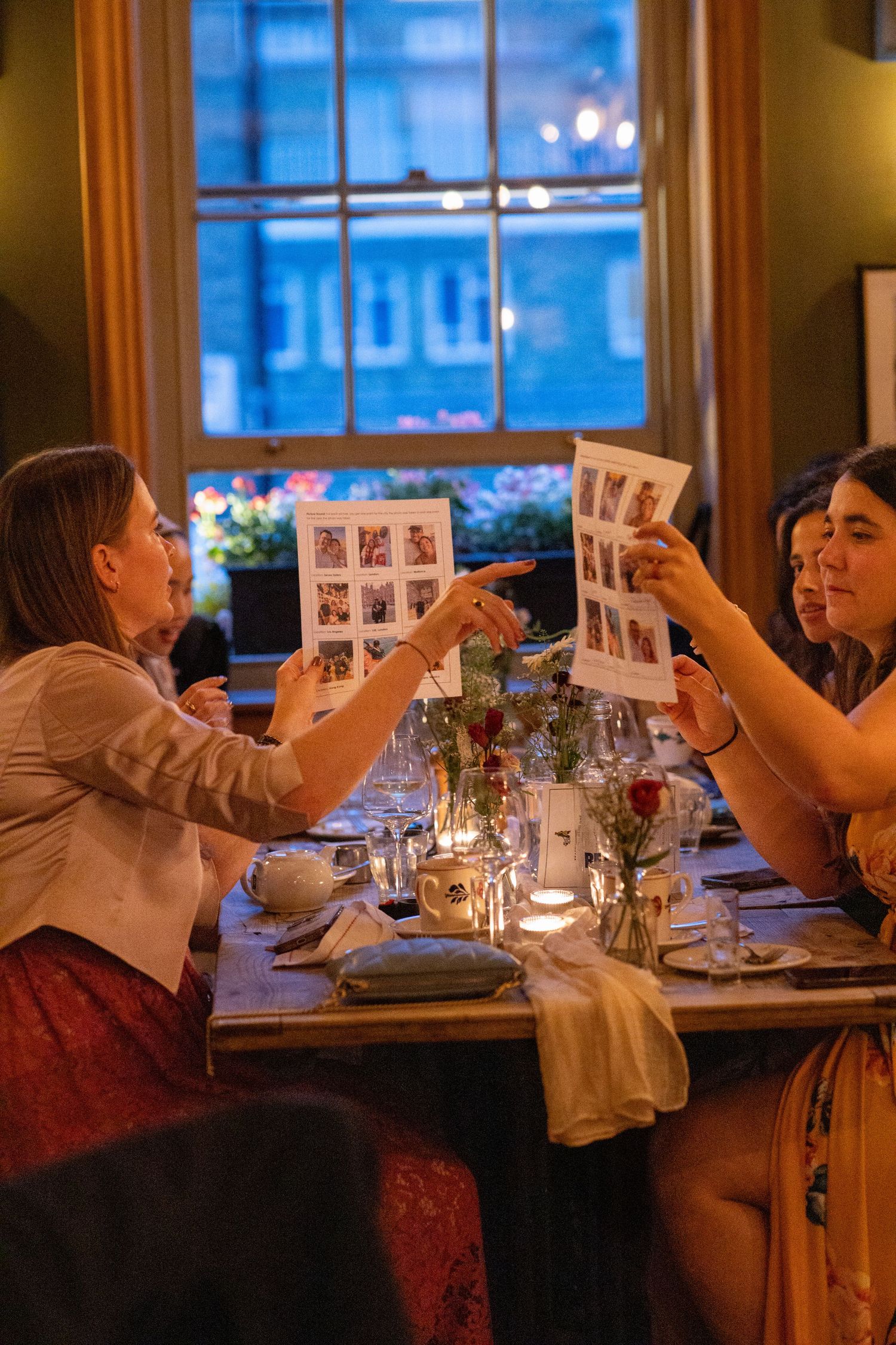 Wedding guests reviewing photo strips at candlelit dinner reception table.