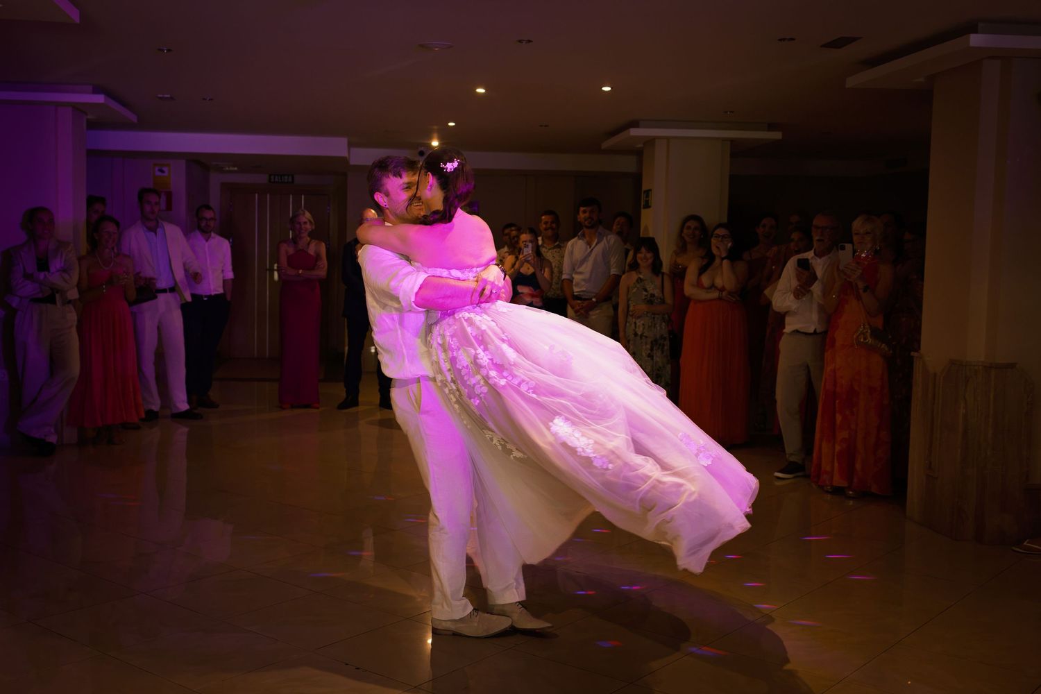 Groom lifts bride in stunning wedding dress during romantic first dance at reception.