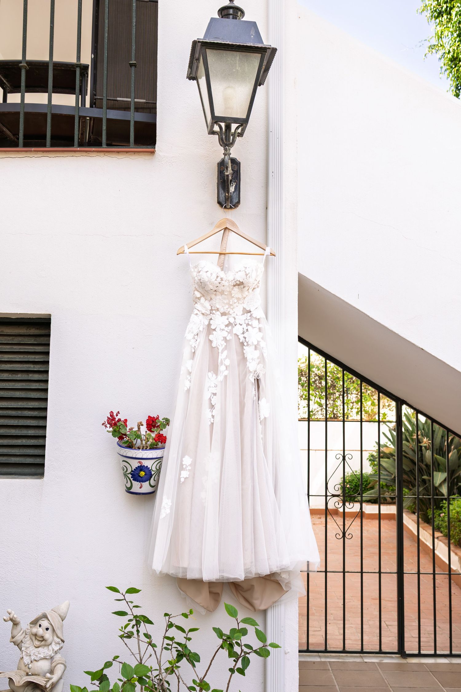 Elegant floral applique wedding dress hanging on a wooden hanger outside a white Mediterranean villa.